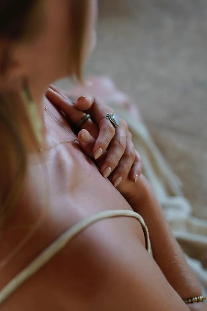 Close-up of a woman touching her chest with her hand, showing jewelry, with a blurred background.