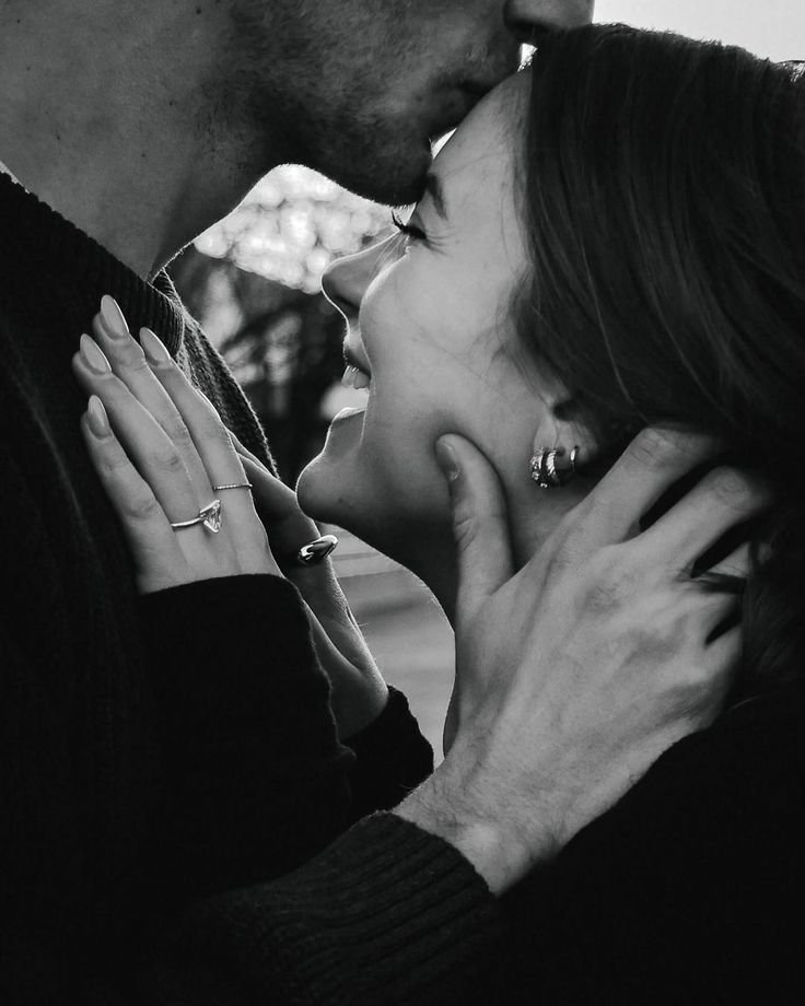 A black-and-white photo of a couple closely embracing outdoors, with the man gently touching the woman's face as they lean in for a kiss.