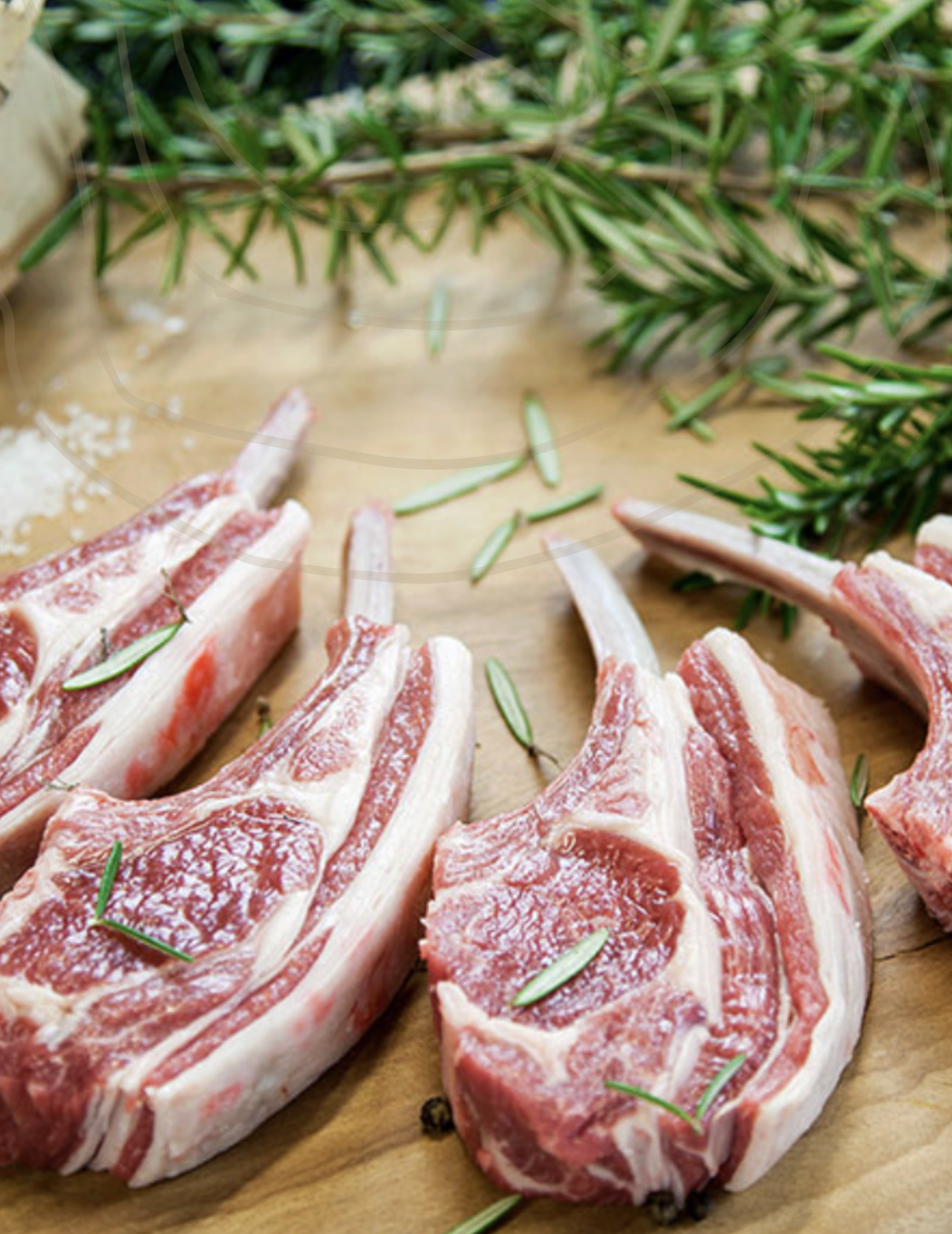 Raw lamb chops with rosemary on a wooden cutting board.