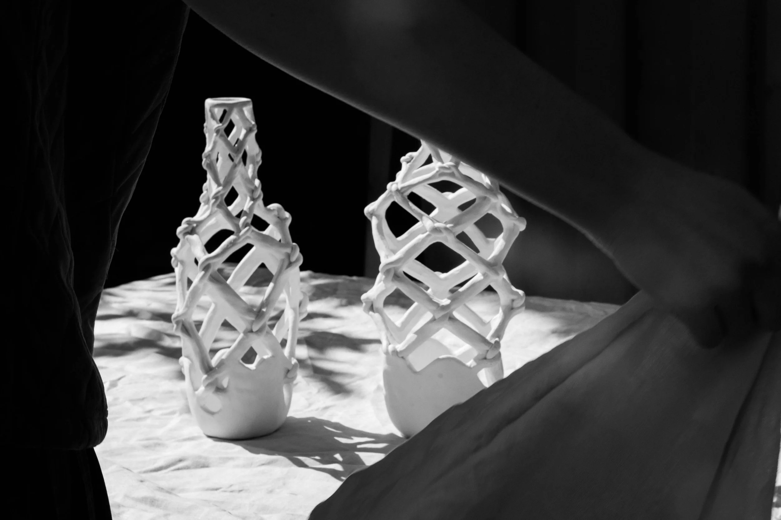 Two decorative white ceramic vases with lattice structures are displayed on a surface, illuminated by light from the side, creating shadows.