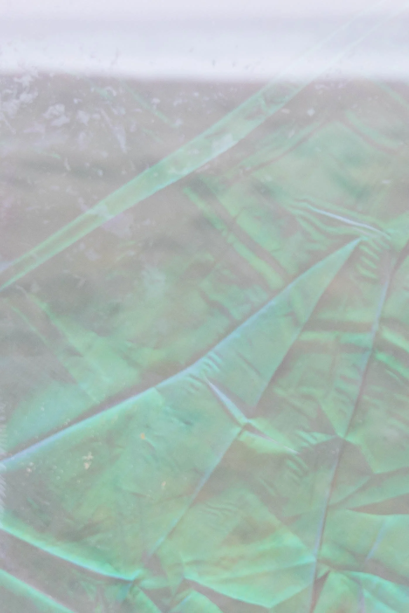 Close-up of an iridescent holographic green fabric with visible crinkles.