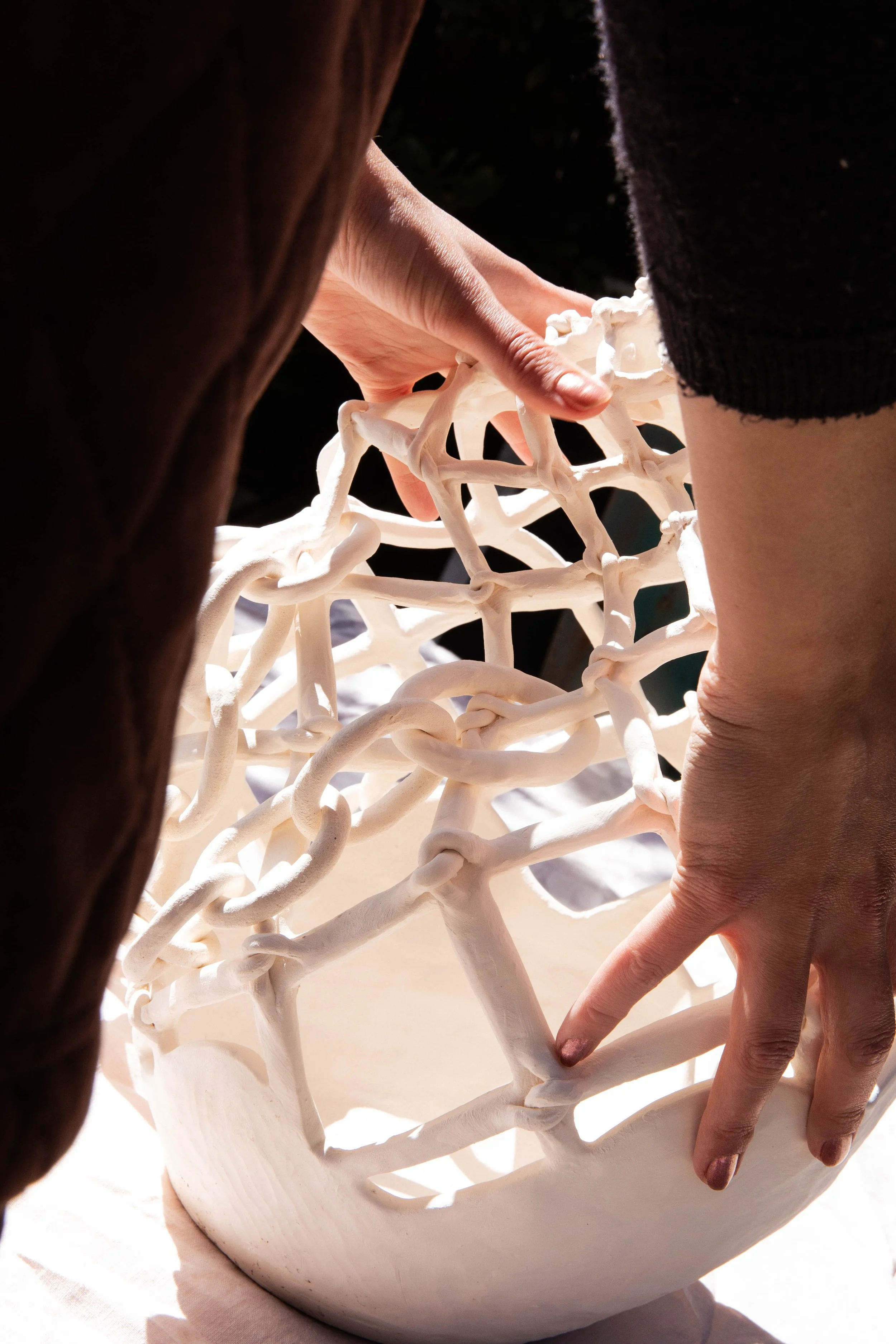 Close-up of two hands adjusting a white ceramic sculpture resembling a tangled web on a round base.