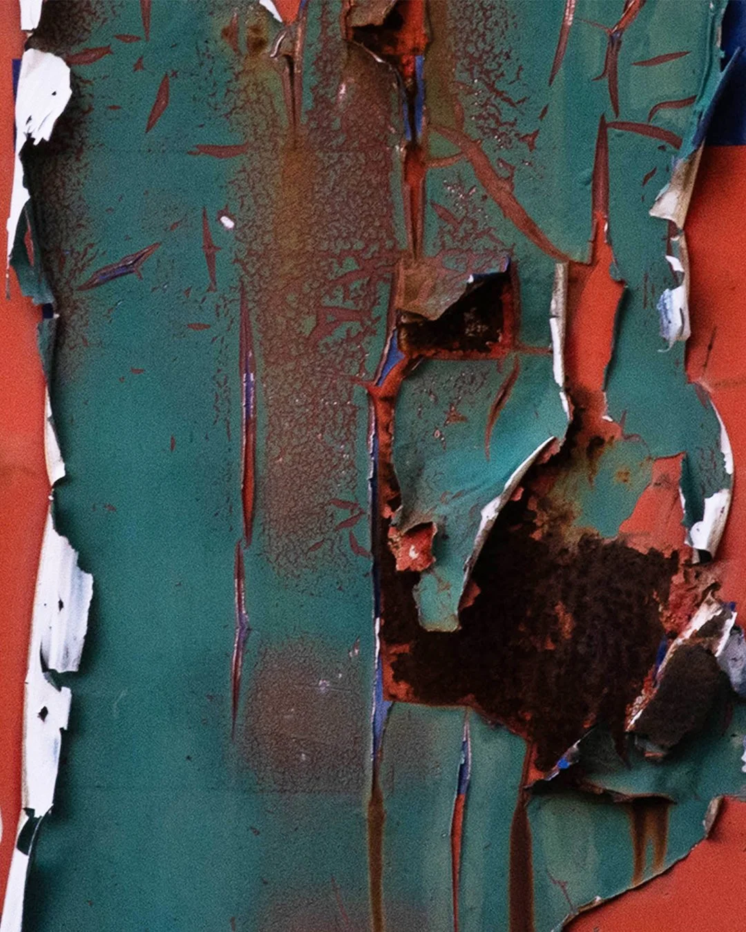 Close-up of a torn, rusted, and peeling painted metal surface with layers of green, brown, and white paint, and areas of rust and corrosion.