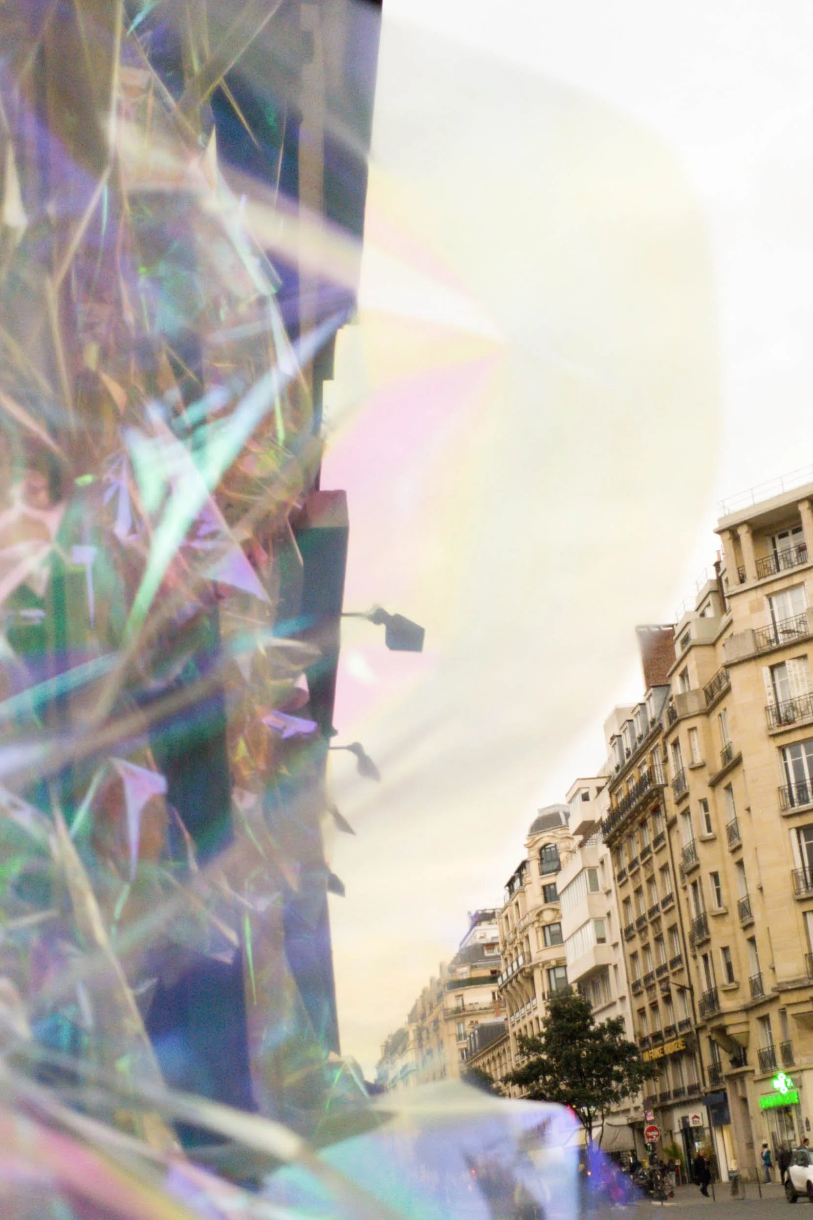 An urban street scene with multi-story buildings and a lamppost. Foreground shows iridescent, holographic material reflecting light.