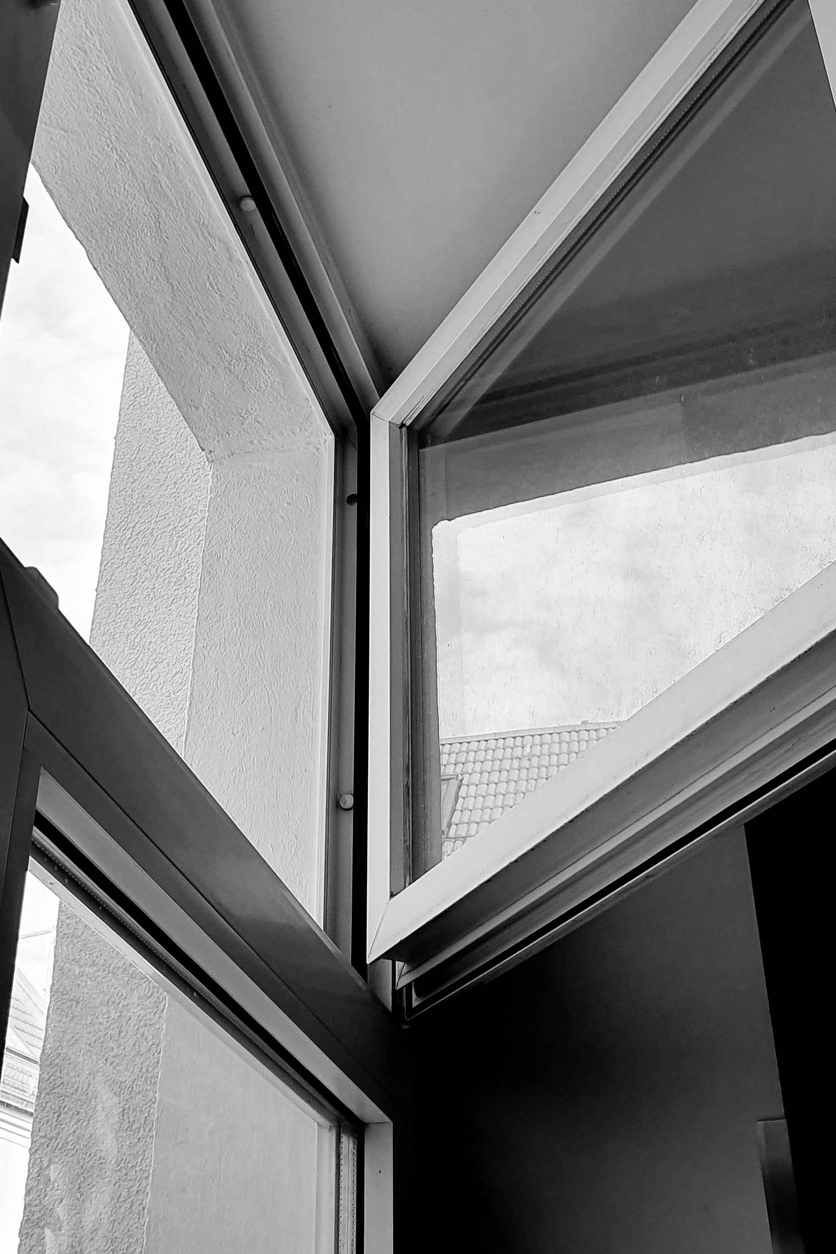 Black and white photo of an open window with a view of a tiled roof outside.