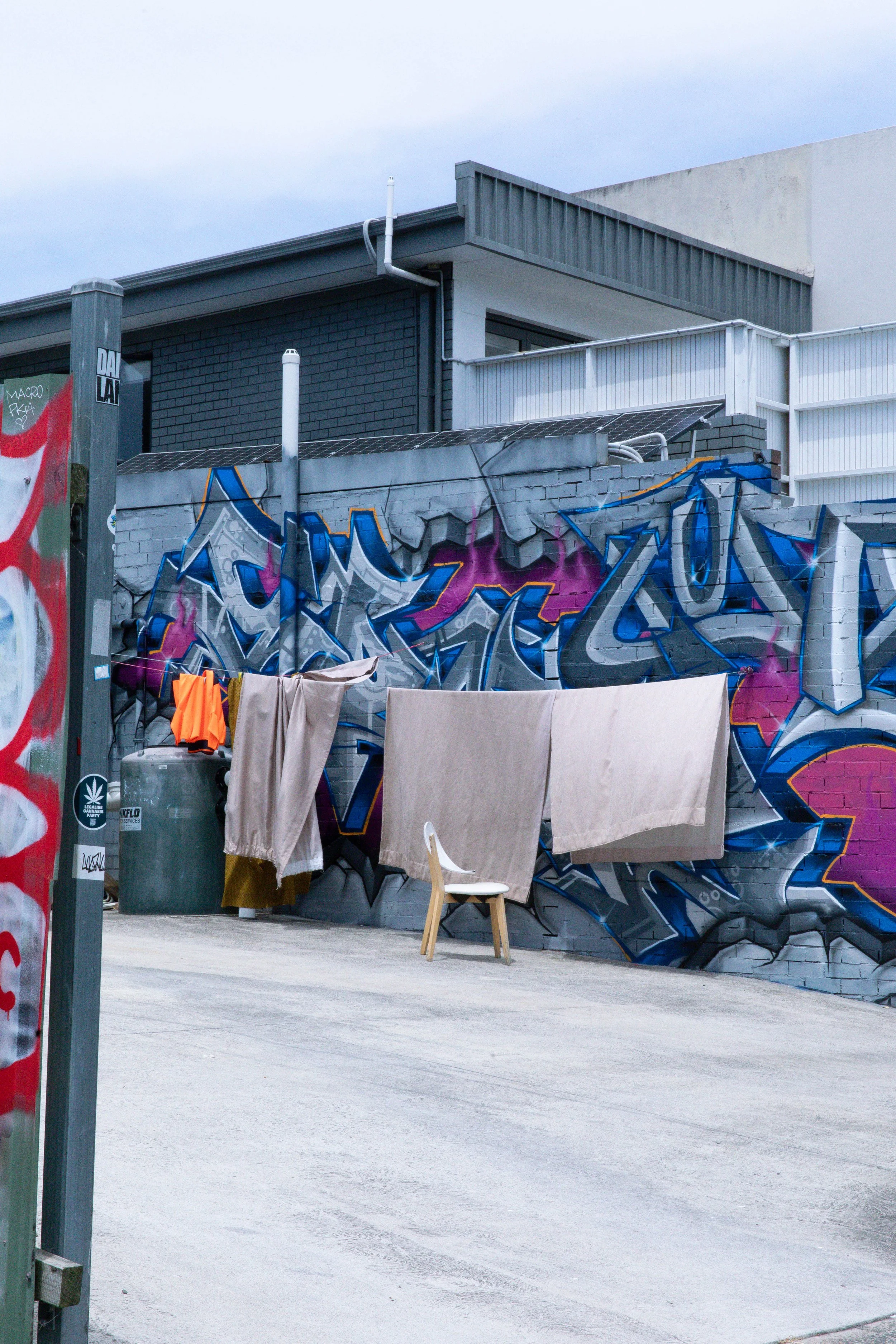 Graffiti art on a brick wall, with laundry hanging on a clothesline and a small chair in front.