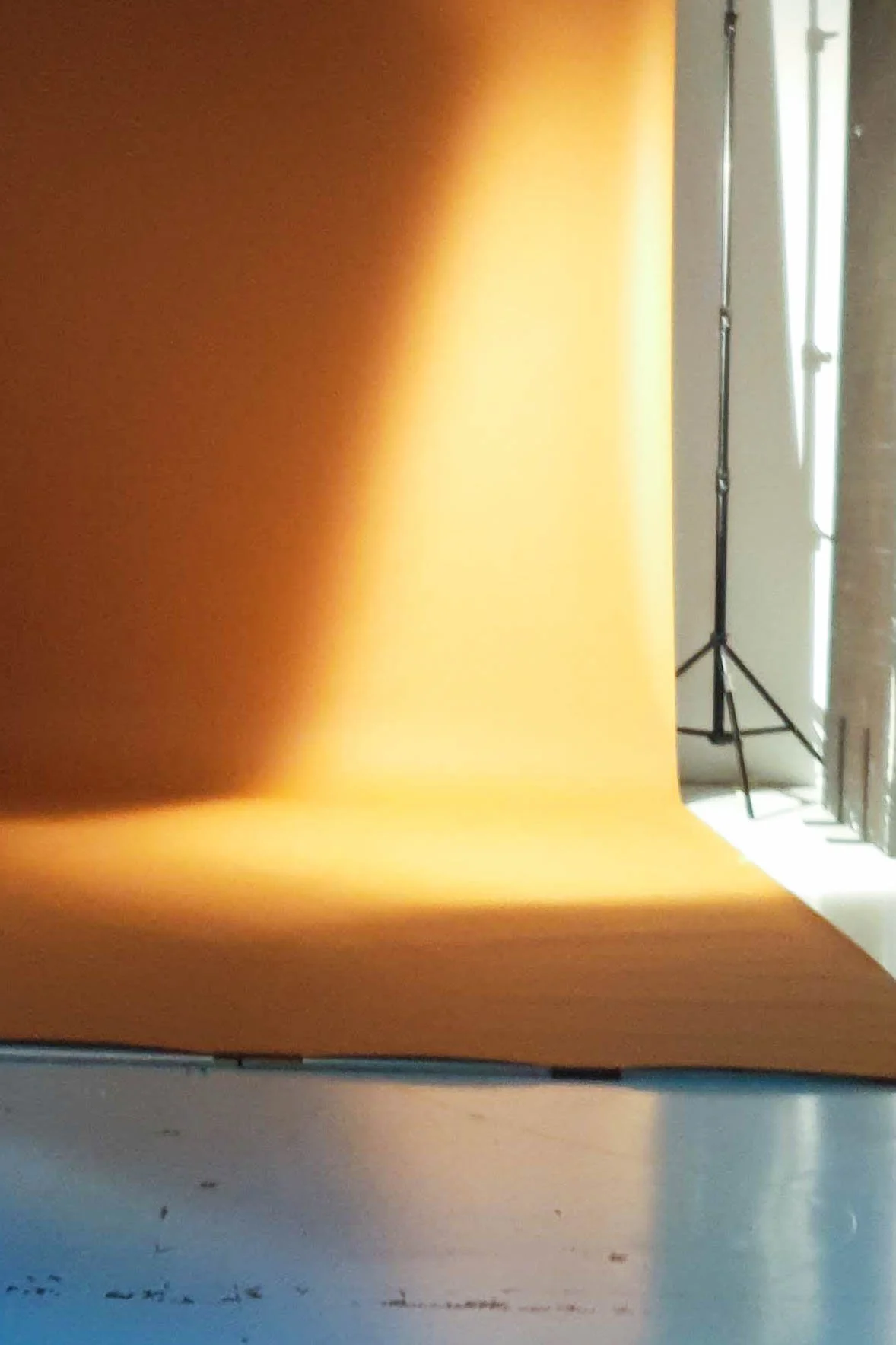 A bright yellow backdrop in a photography studio, with a tripod and light stand visible on the right side.