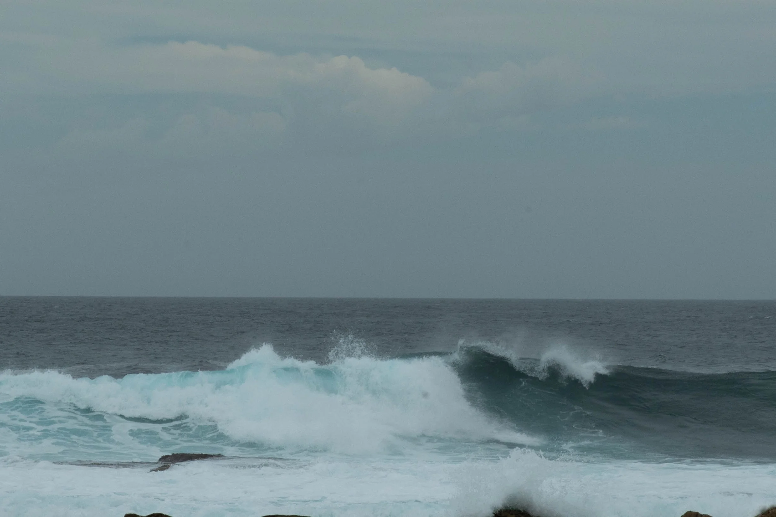 Ocean waves crashing against rocks under a cloudy sky.