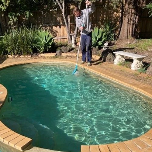Person cleaning a small backyard swimming pool with a net.