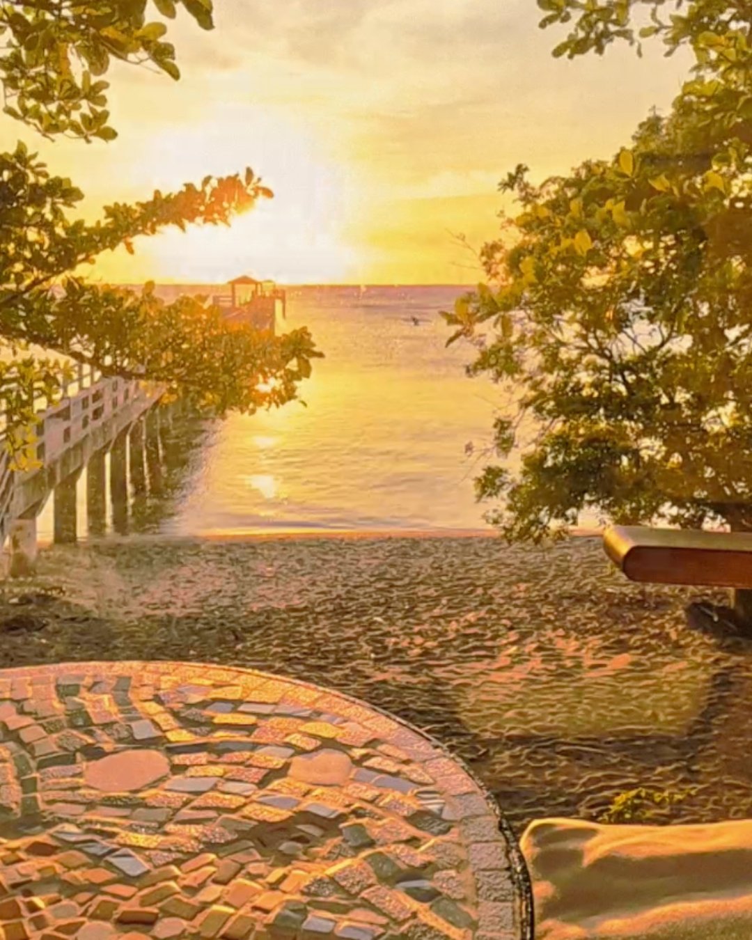 Wooden sign for Tres Marias Vacation Homes with a carved design of two women's faces, a house, a boat, a sun, and palm trees, set against a stone wall background surrounded by colorful plants.