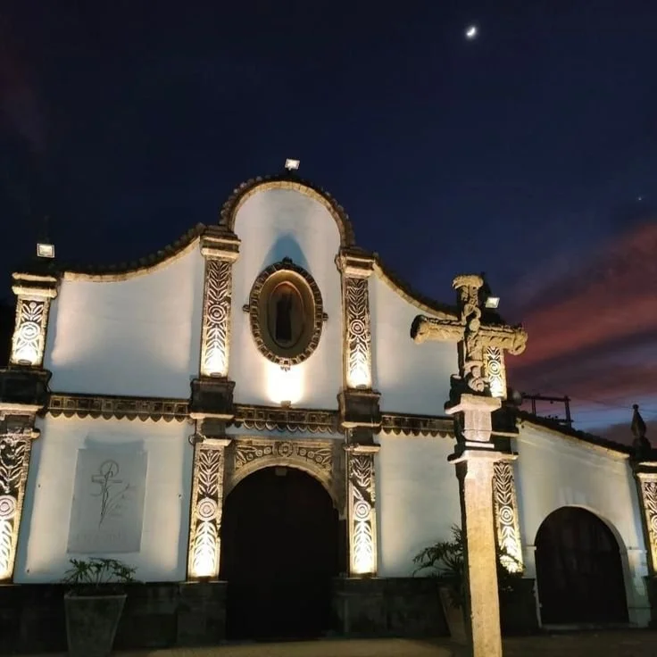Nighttime view of a historic church with ornate architectural details, illuminated from below, with a crescent moon and dark sky in the background.