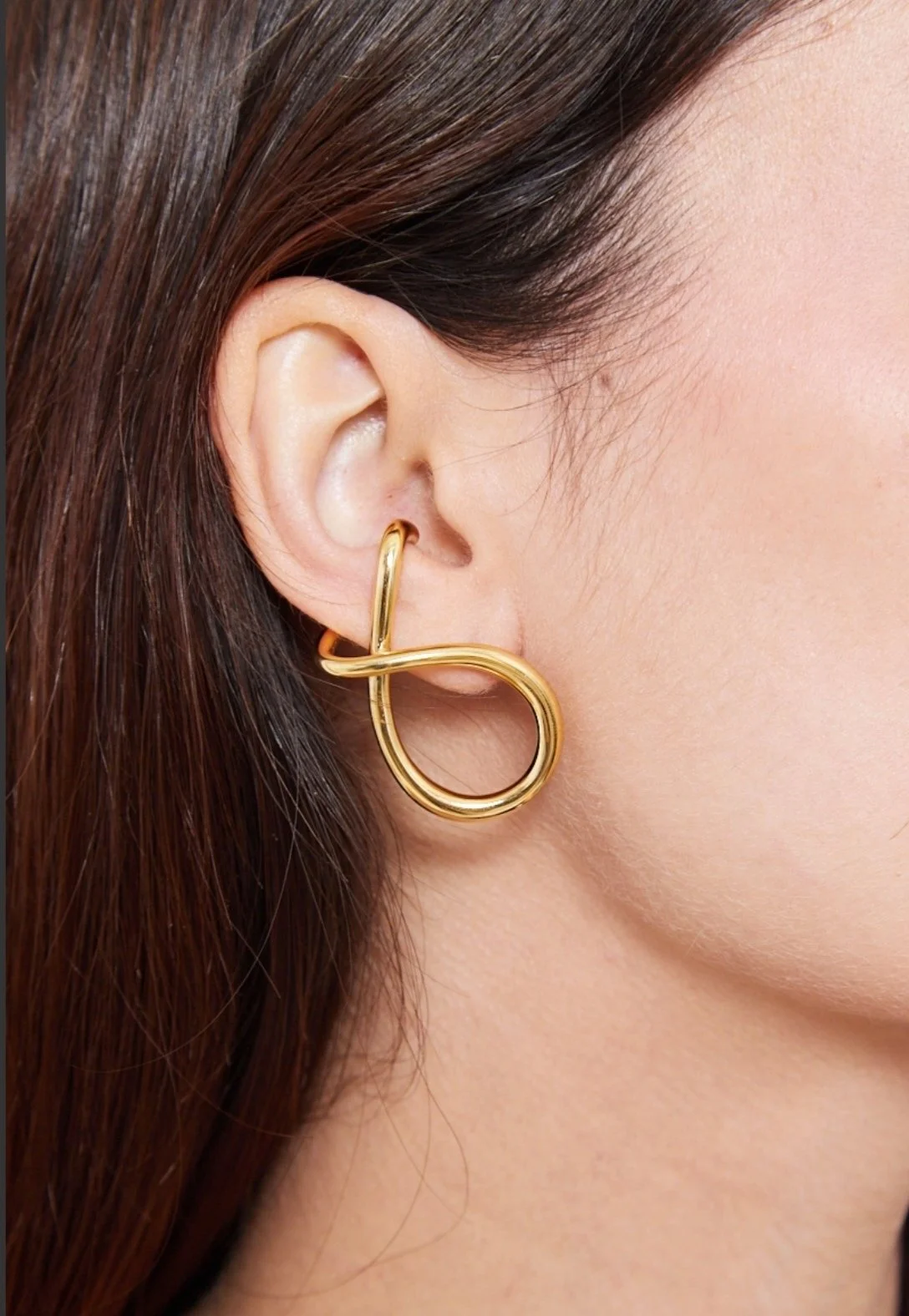 Une grosse boucle d'oreille en or portée dans l'oreille d'une femme avec les cheveux bruns