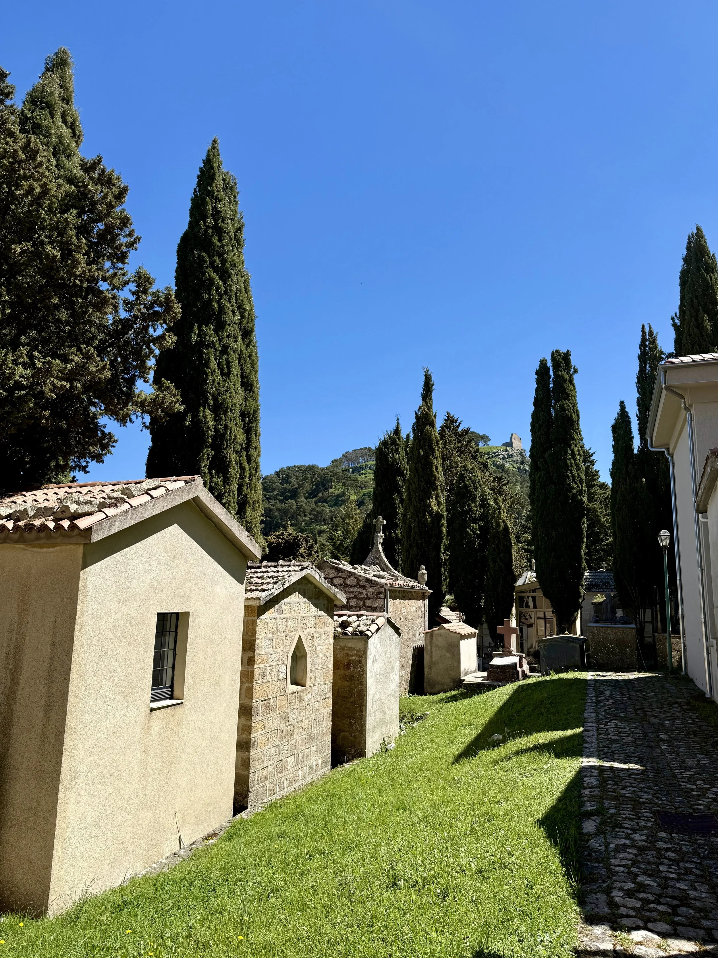Geraci Siculo Cemetery on a bright sunny day with the ruins of the Ventimiglia castle visible on a distant hilltop