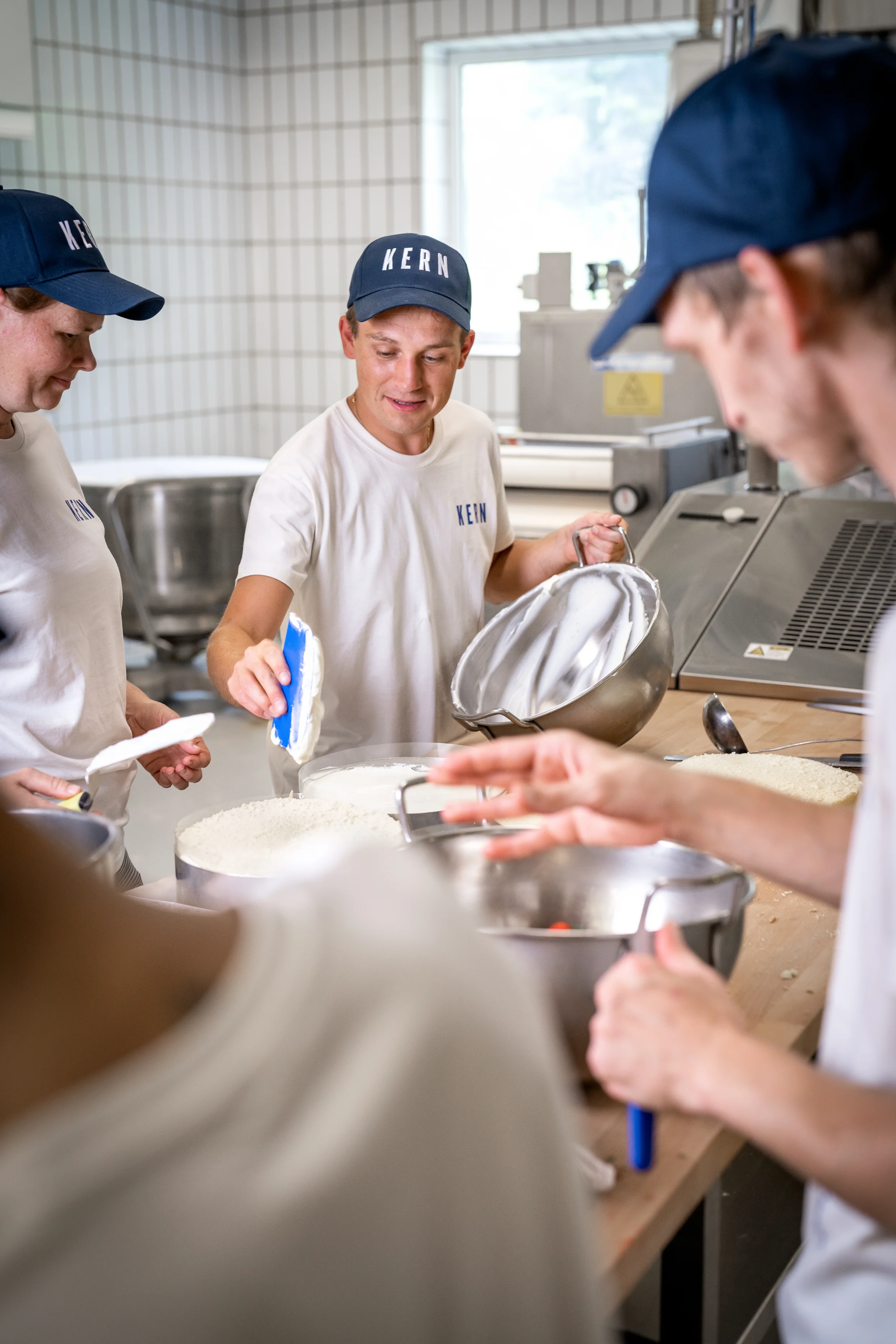 Menschen in weißem T-Shirt und blauer Mütze beim Zubereiten von Speiseeis in einer Küche.