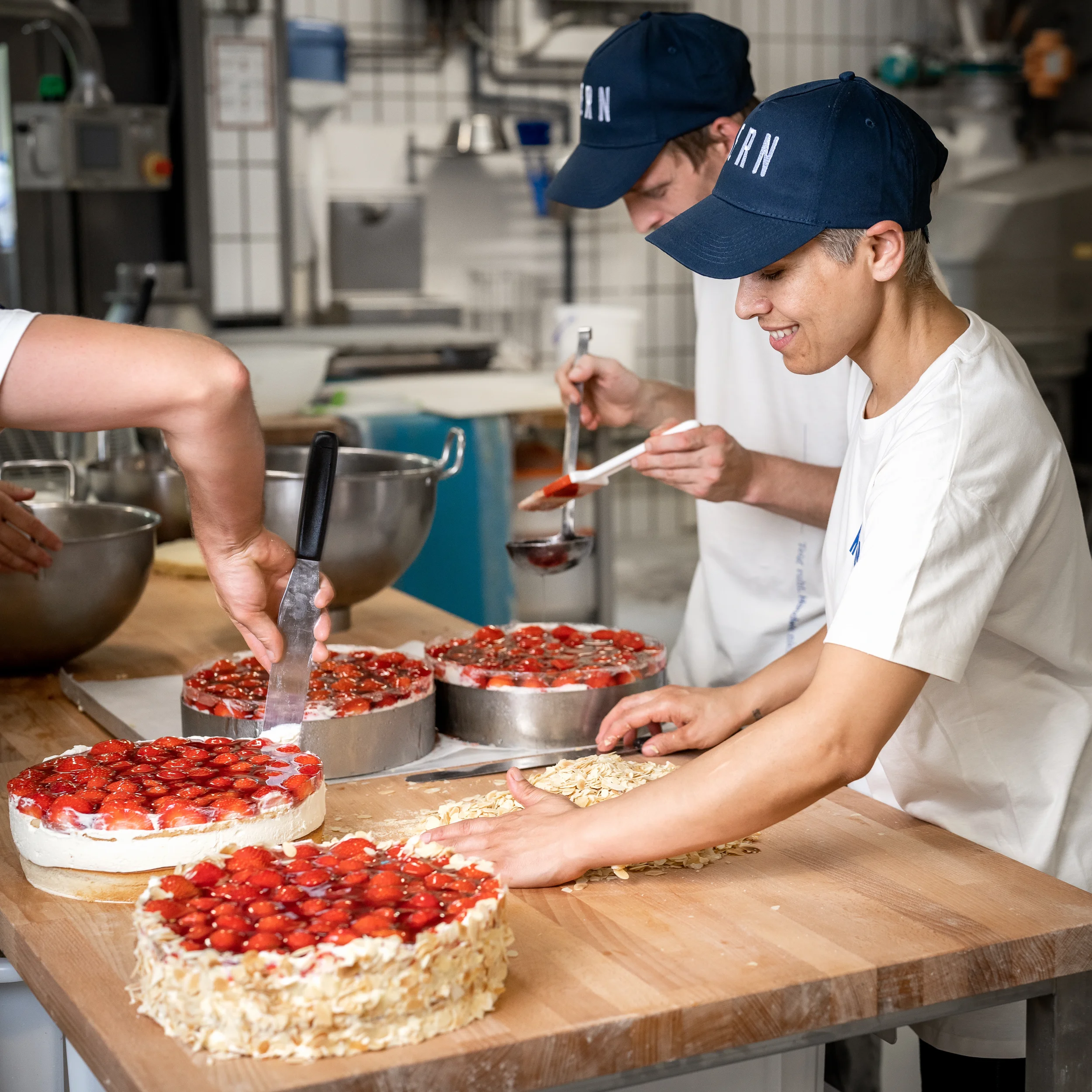 Menschen bereiten Erdbeerkuchen in einer professionellen Backküche vor.