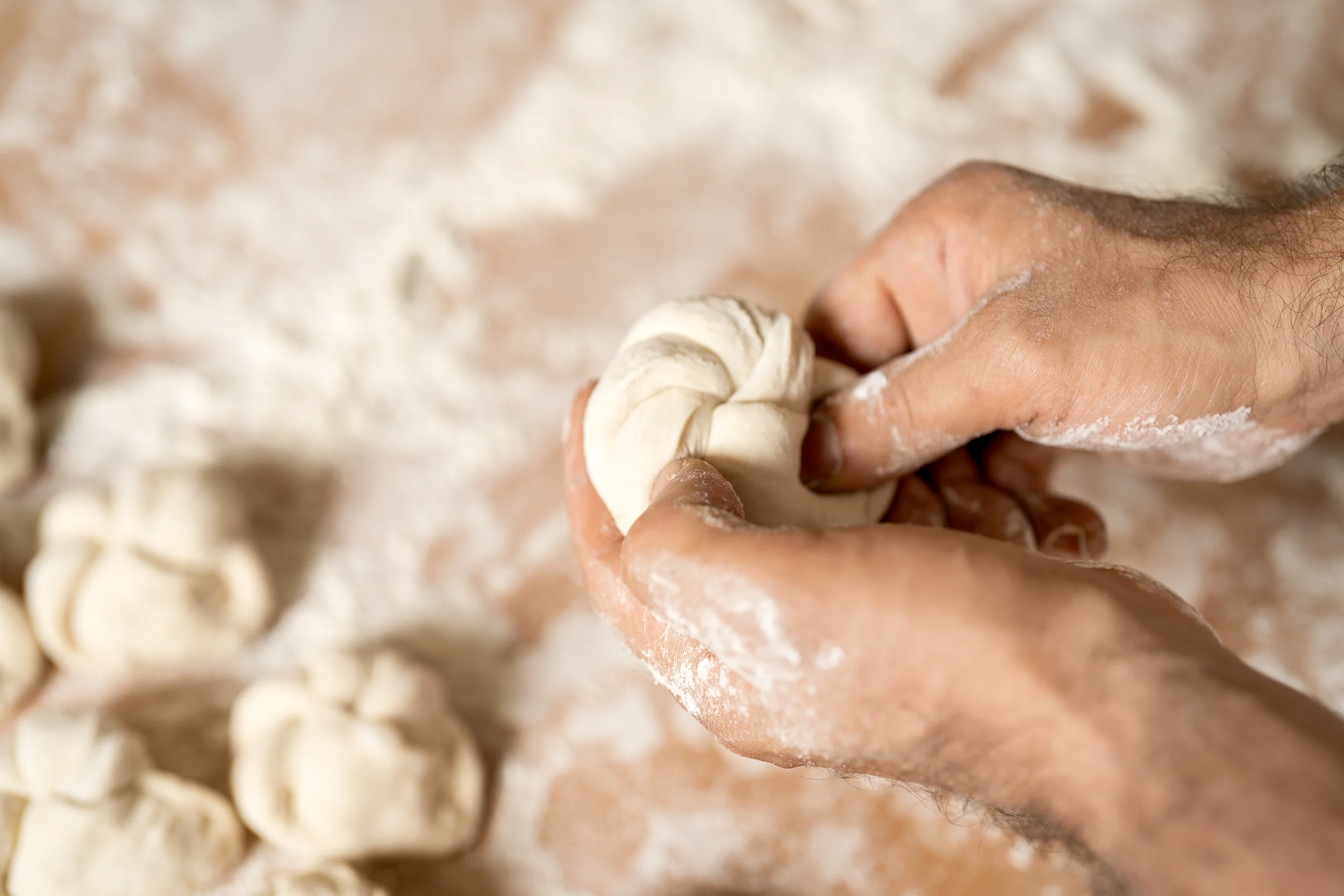 Hand formt Teig zu Handsemmel auf einer bemehlten Oberfläche.