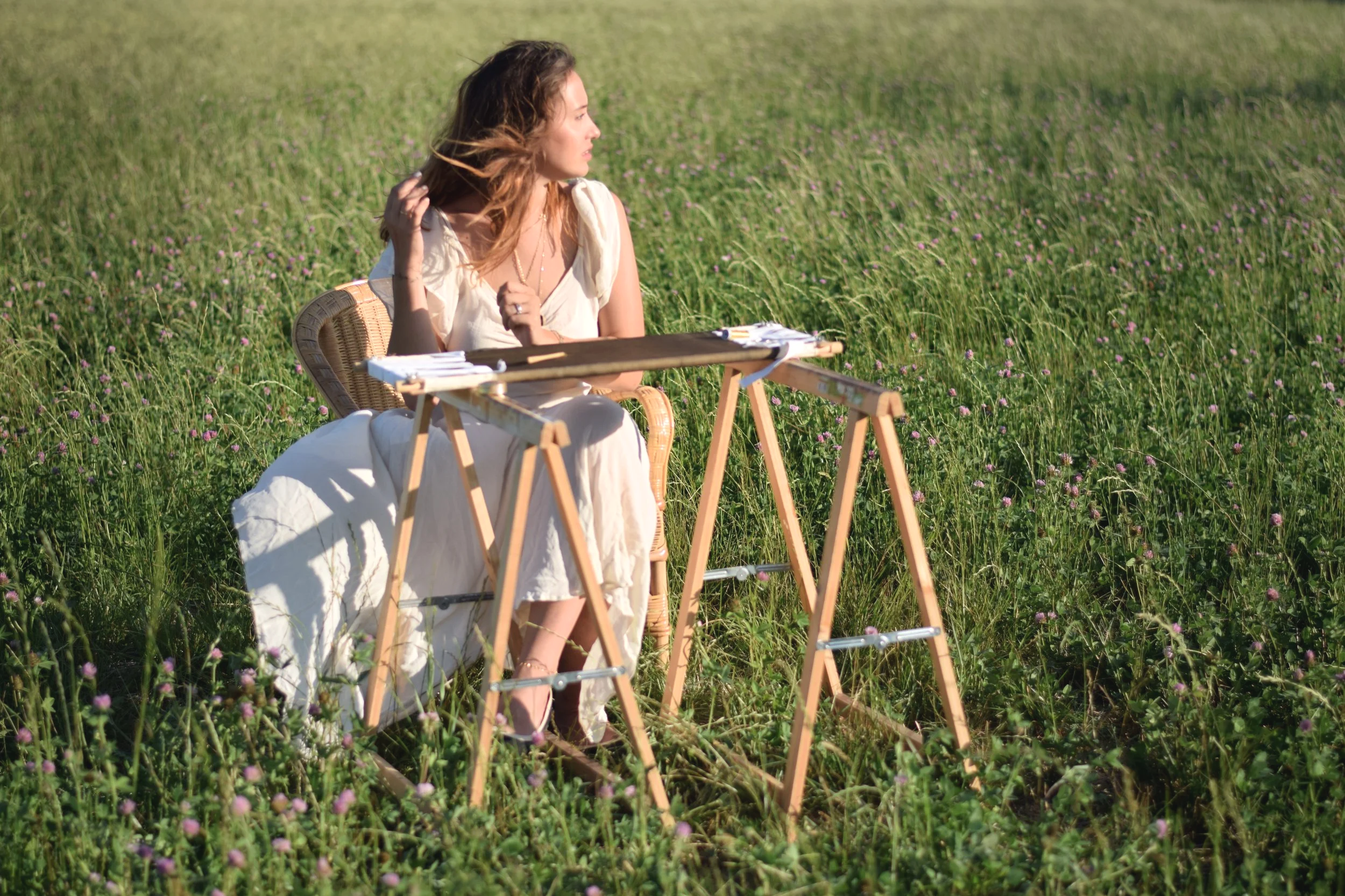 Une femme assise dans un champ de fleurs, regardant vers la droite, avec une table en bois devant elle.