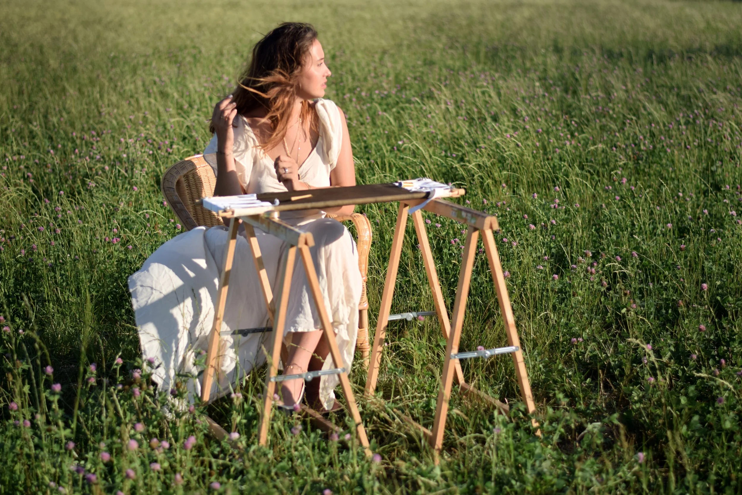 Femme assise dans un champ de fleurs, brodant sur une toile avec des tréteaux en bois.