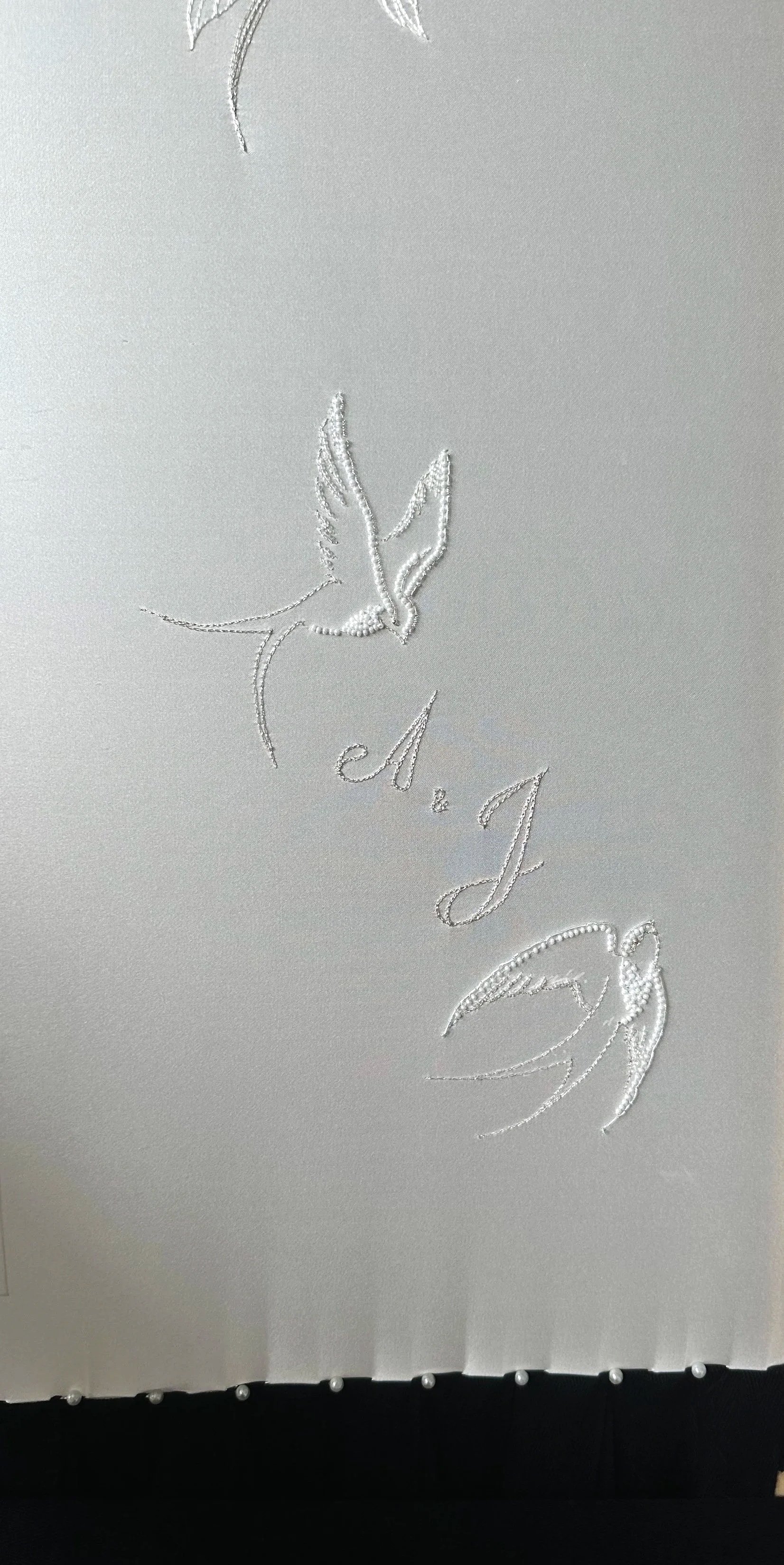 Tissu blanc avec broderie de deux oiseaux stylisés et les initiales M.J.