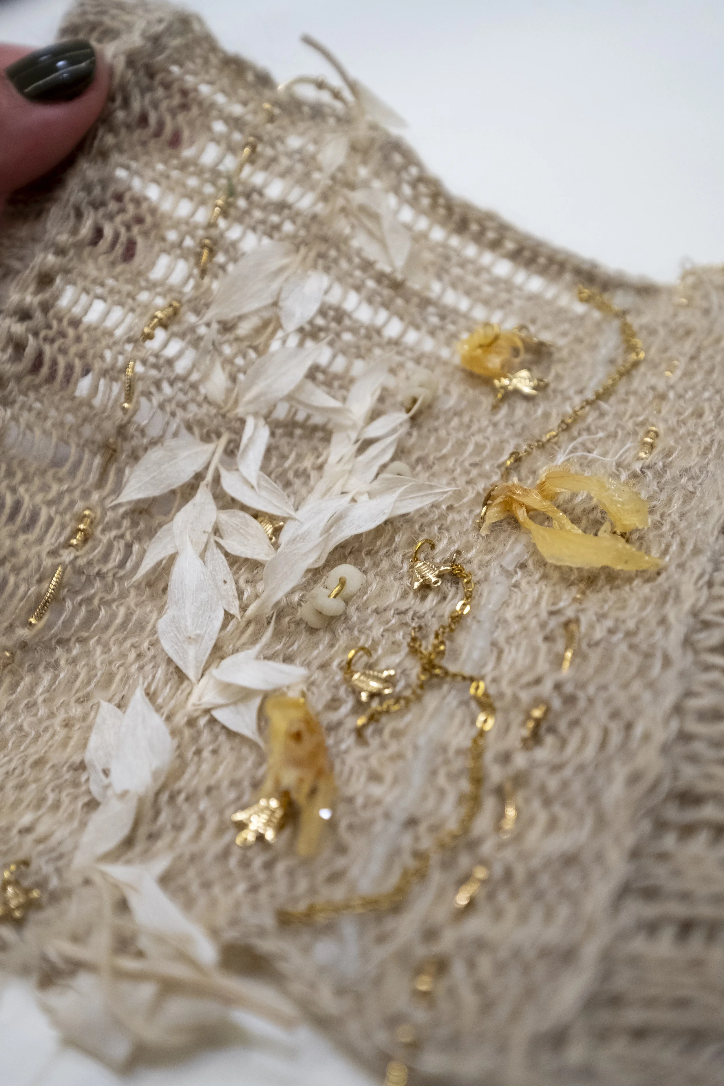 Tricot contenant des bijoux en or, comme des chaînes, des anneaux et des pendentifs, accompagnée de fleurs séchées