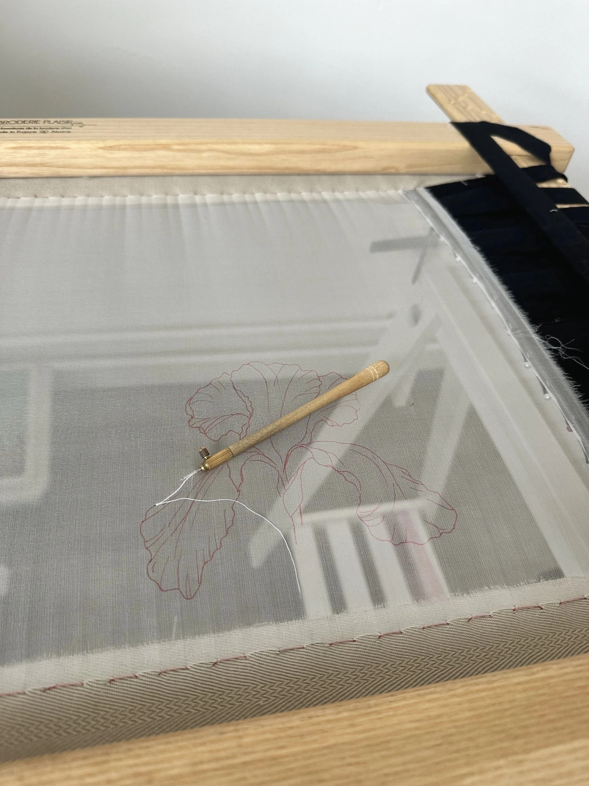 Une machine à broder avec un motif floral en cours de réalisation. Le motif est de couleur rouge et se trouve sur un tissu transparent.