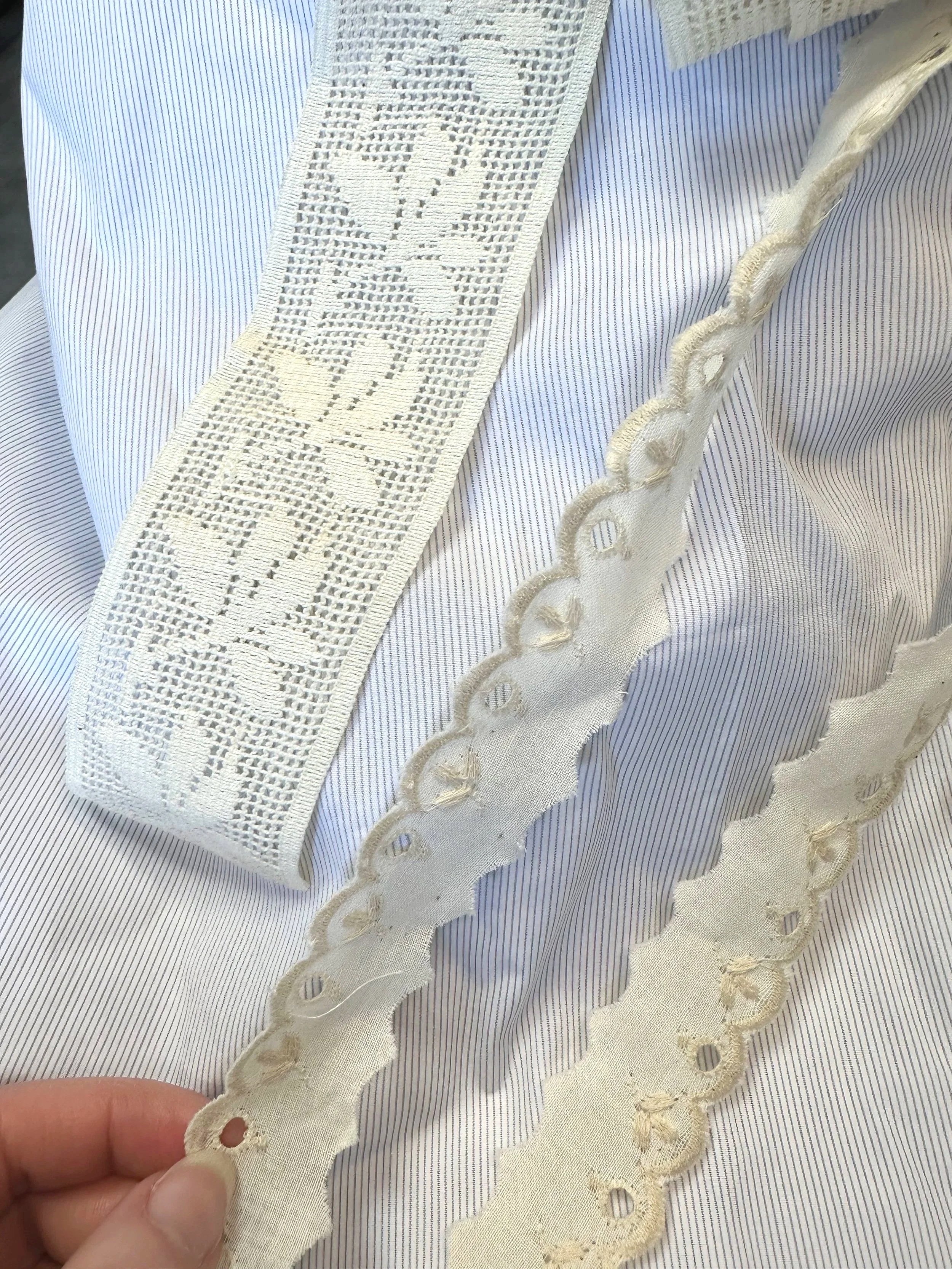 Zoom sur un tissu en dentelle blanche avec des motifs floraux au bord d'un vêtement en tissu rayé bleu et blanc.