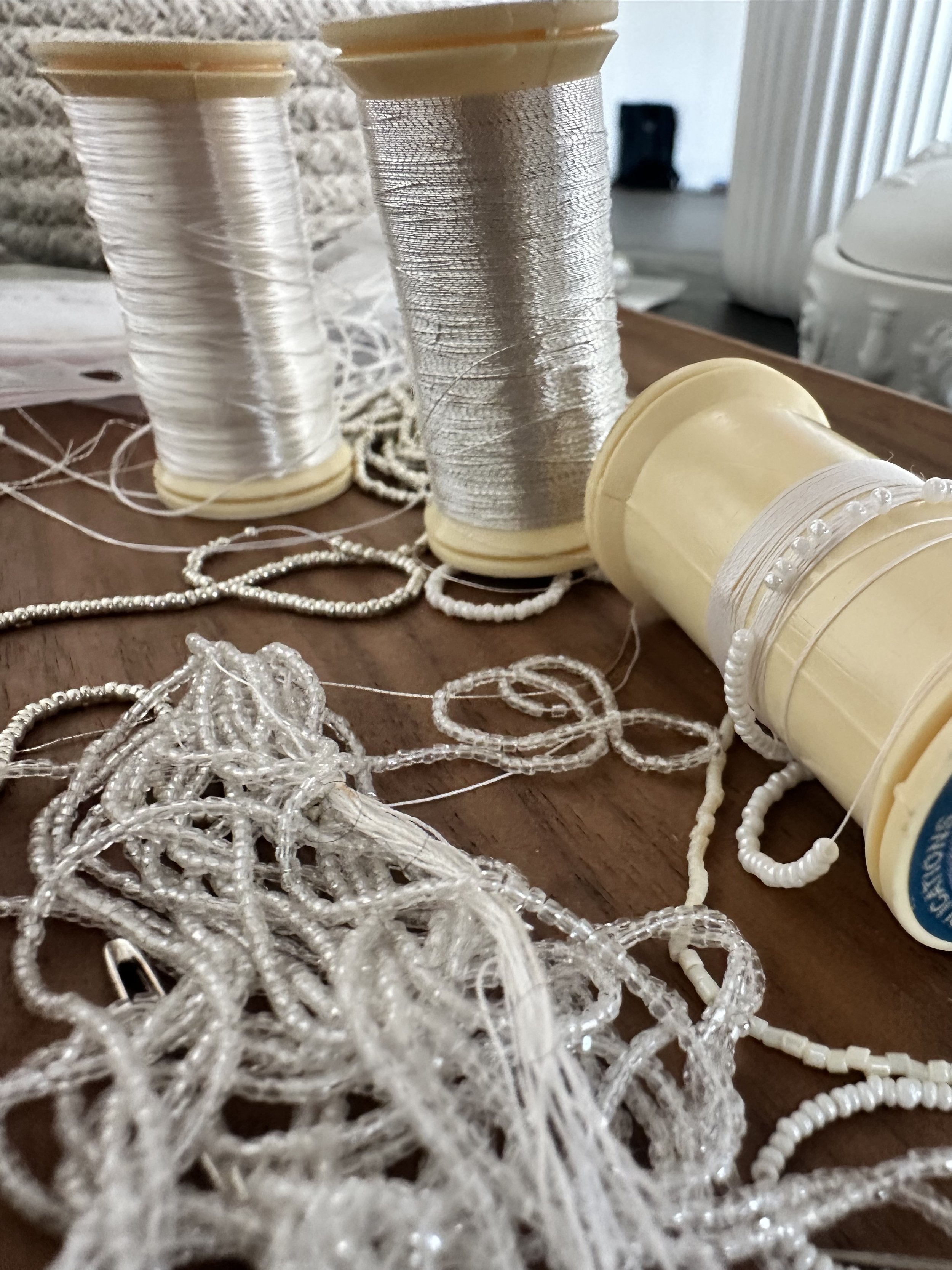 Bobines de fil en plastique blanc et perles blanches, avec des morceaux de fil entremêlés, sur une surface en bois.