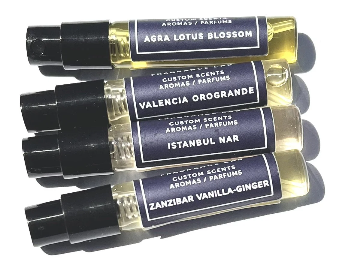 Four small perfume bottles with black caps and purple labels reading 'Agra Lotus Blossom,' 'Valencia Orogrande,' 'Istanbul Nar,' and 'Zanzibar Vanilla-Ginger.'