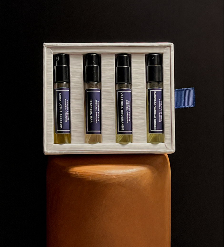 A box containing four small bottles labeled with different essential oil scents, placed on a brown surface against a dark background.