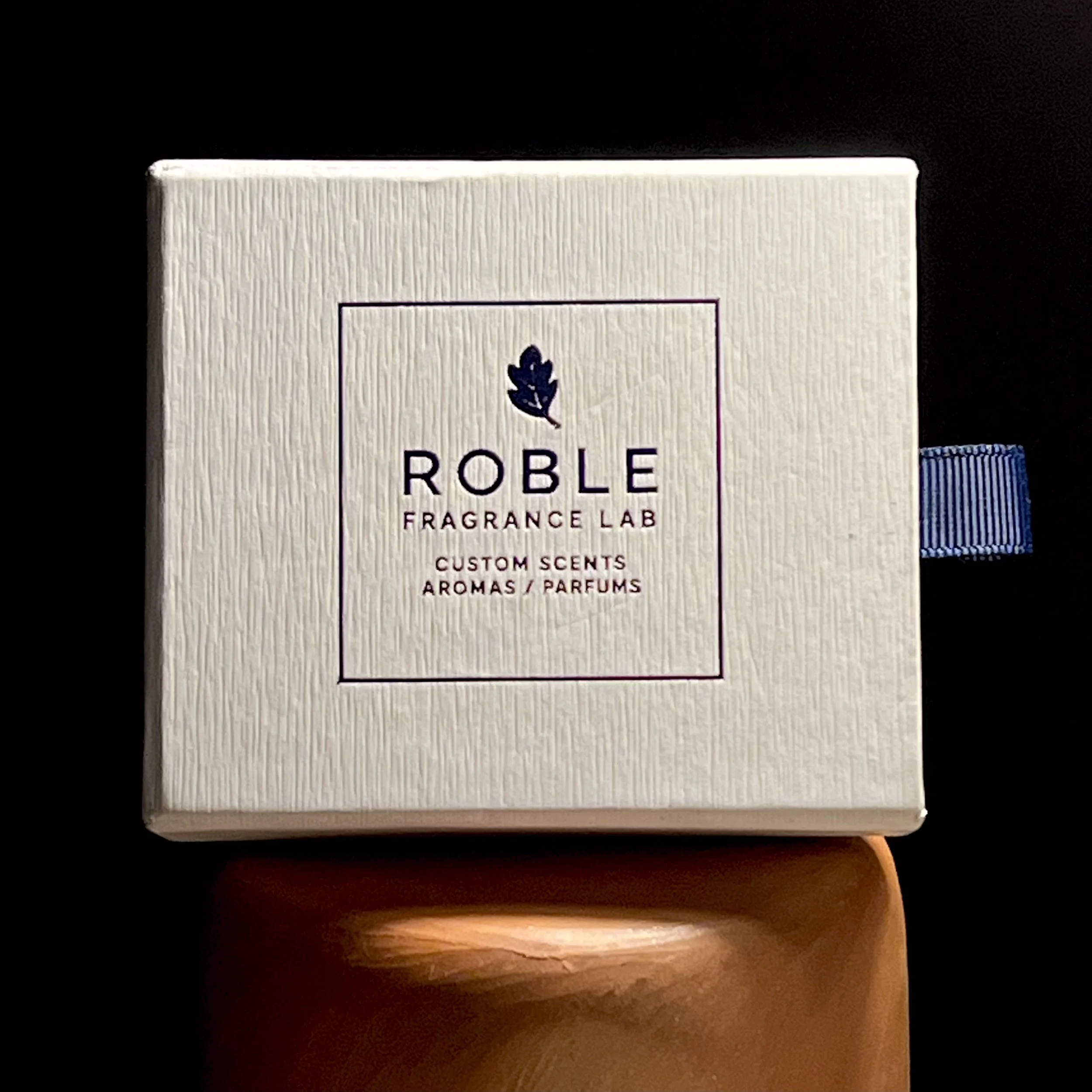 Close-up of a product box with the label 'Poble Fragrance Lab' on a black and wood surface.