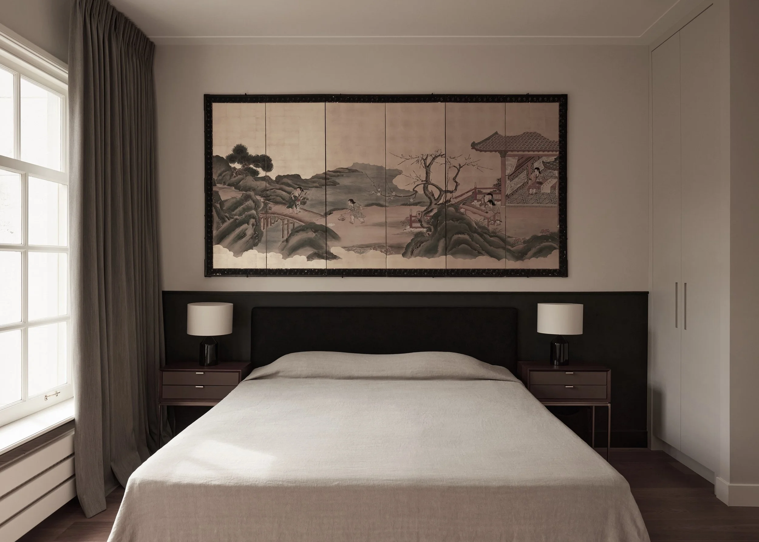 Minimalist bedroom with Asian painting above a bed, gray curtains, side tables, and lamps.