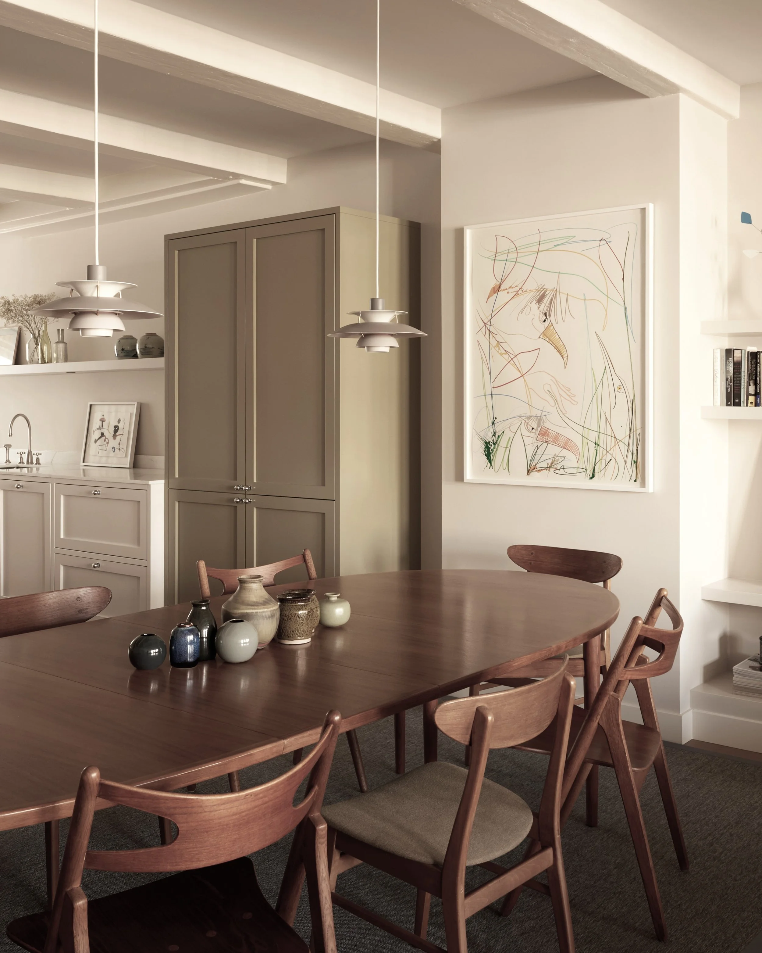 Modern dining room with wooden table and chairs, ceramic vases, abstract wall art, pendant lights, and minimalist decor.