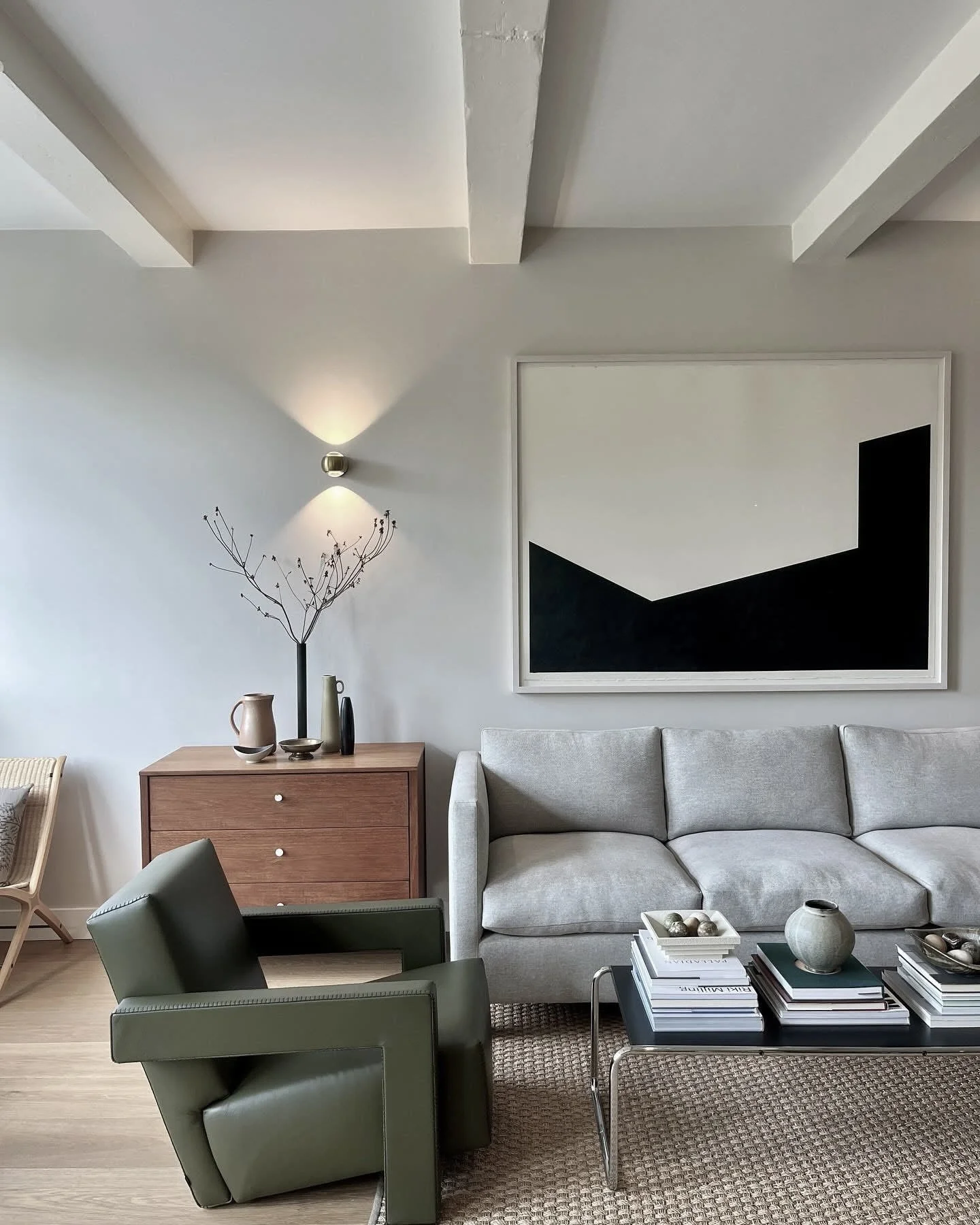 Modern living room with green armchair, gray sofa, wooden sideboard, abstract art, and coffee table with books and decor.