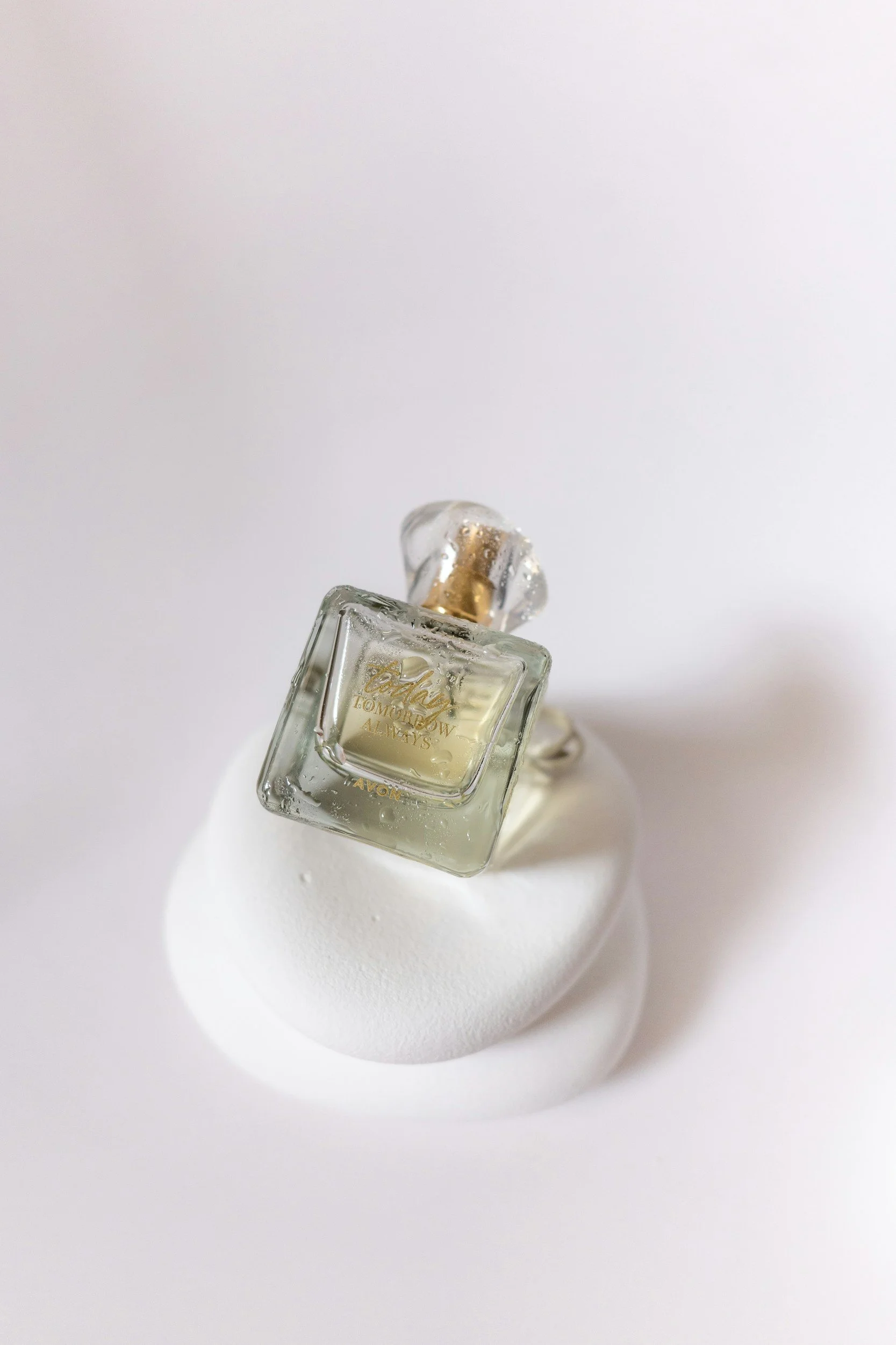 Clear glass perfume bottle with gold accents on a white textured surface.