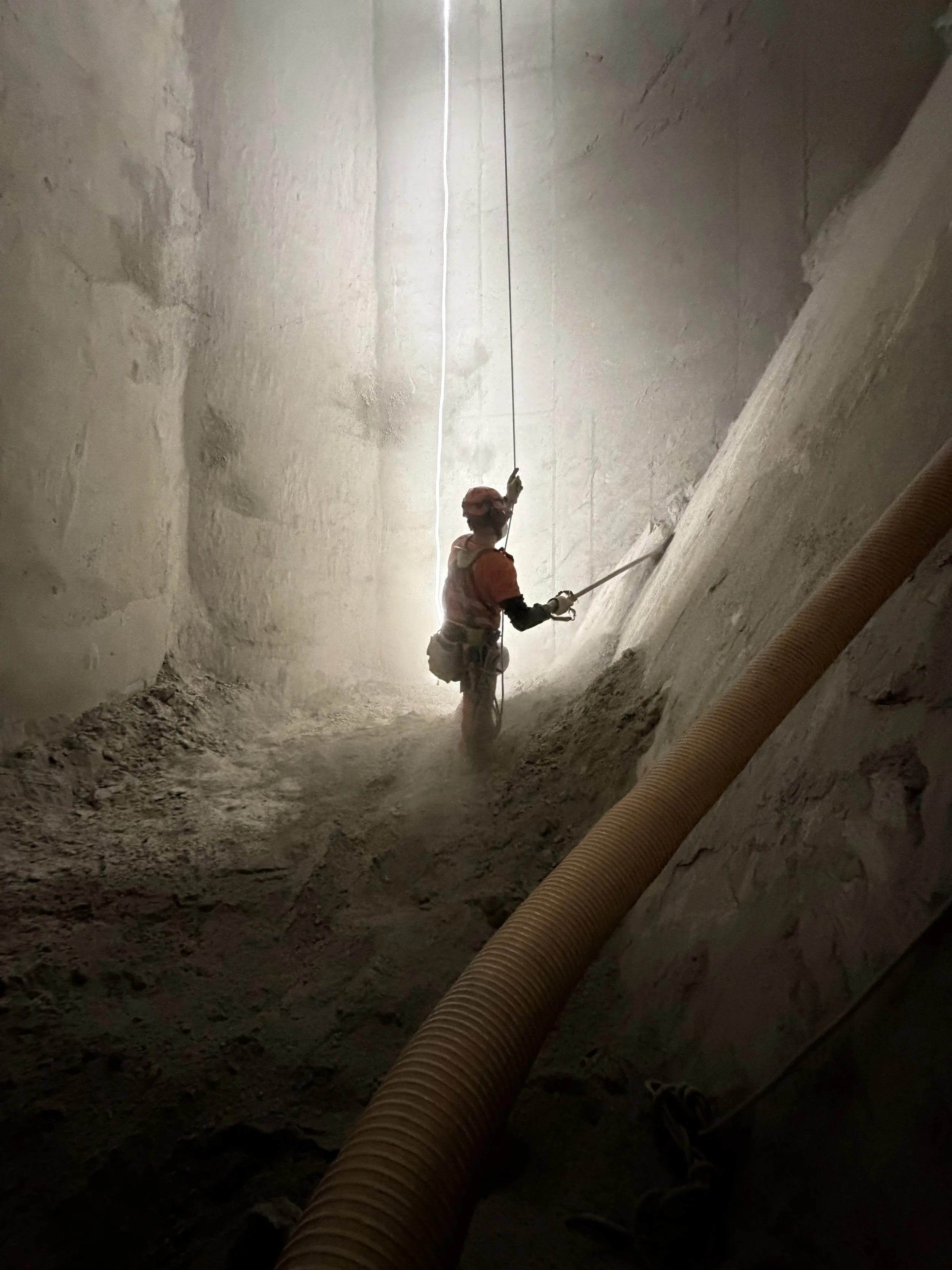 Kletterarbeiter in einem engen, belüfteten Tunnel mit Staub in der Luft.