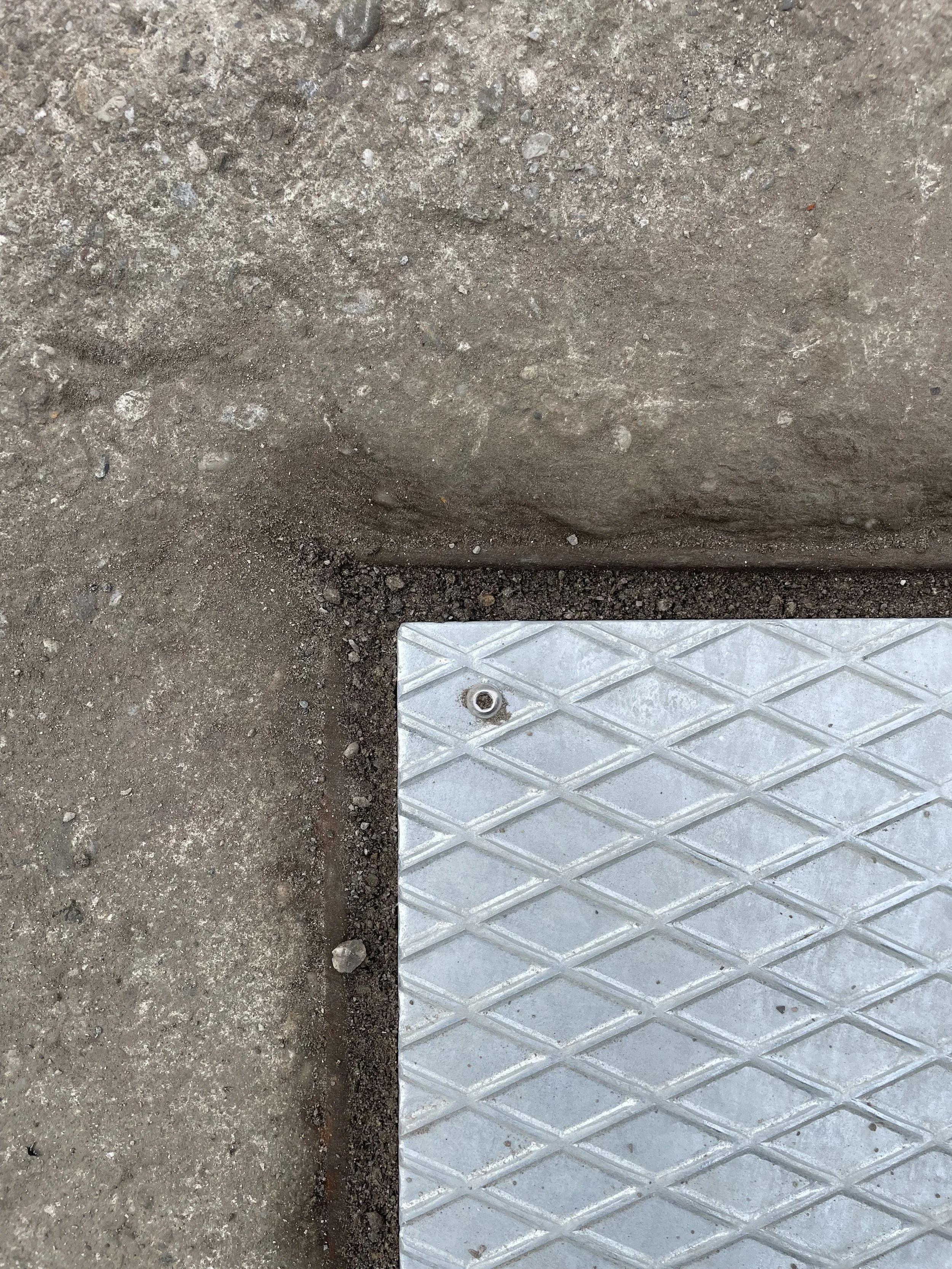 Ein Fußboden mit einer metallischen Platte, die auf der Erde liegt, neben einer massiven Betonwand.