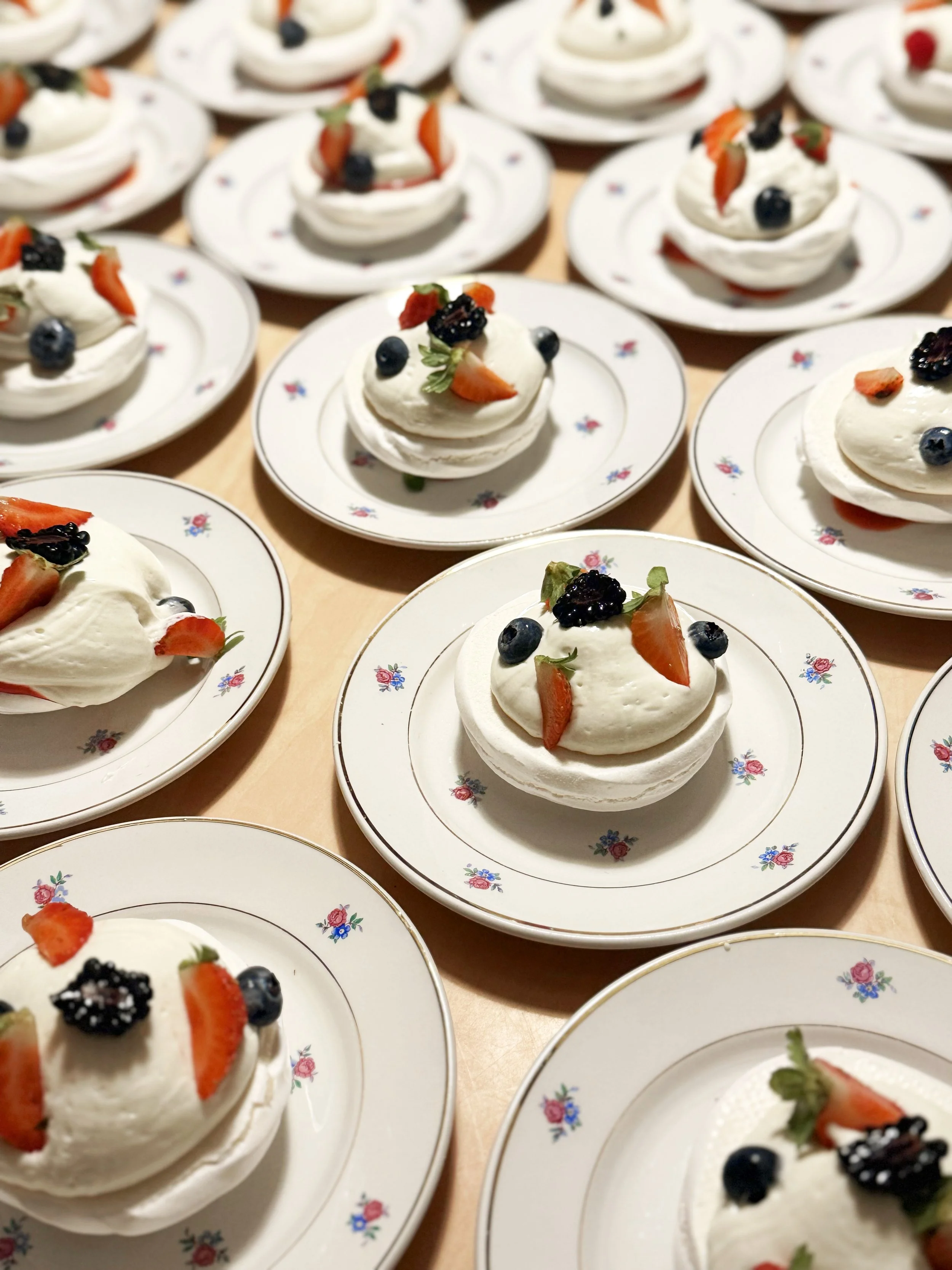 Petites assiettes à desserts contenant des pavlova à la crème garnis de fraises, myrtilles et mûres.