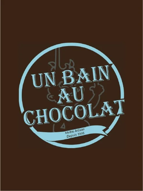 Logo avec texte 'Un Bain au Chocolat', encadré d'un cercle bleu clair sur fond marron, avec un dessin de personnage enfantin en arrière-plan, et une bannière en bas indiquant 'Maître Artisan depuis 1995'.