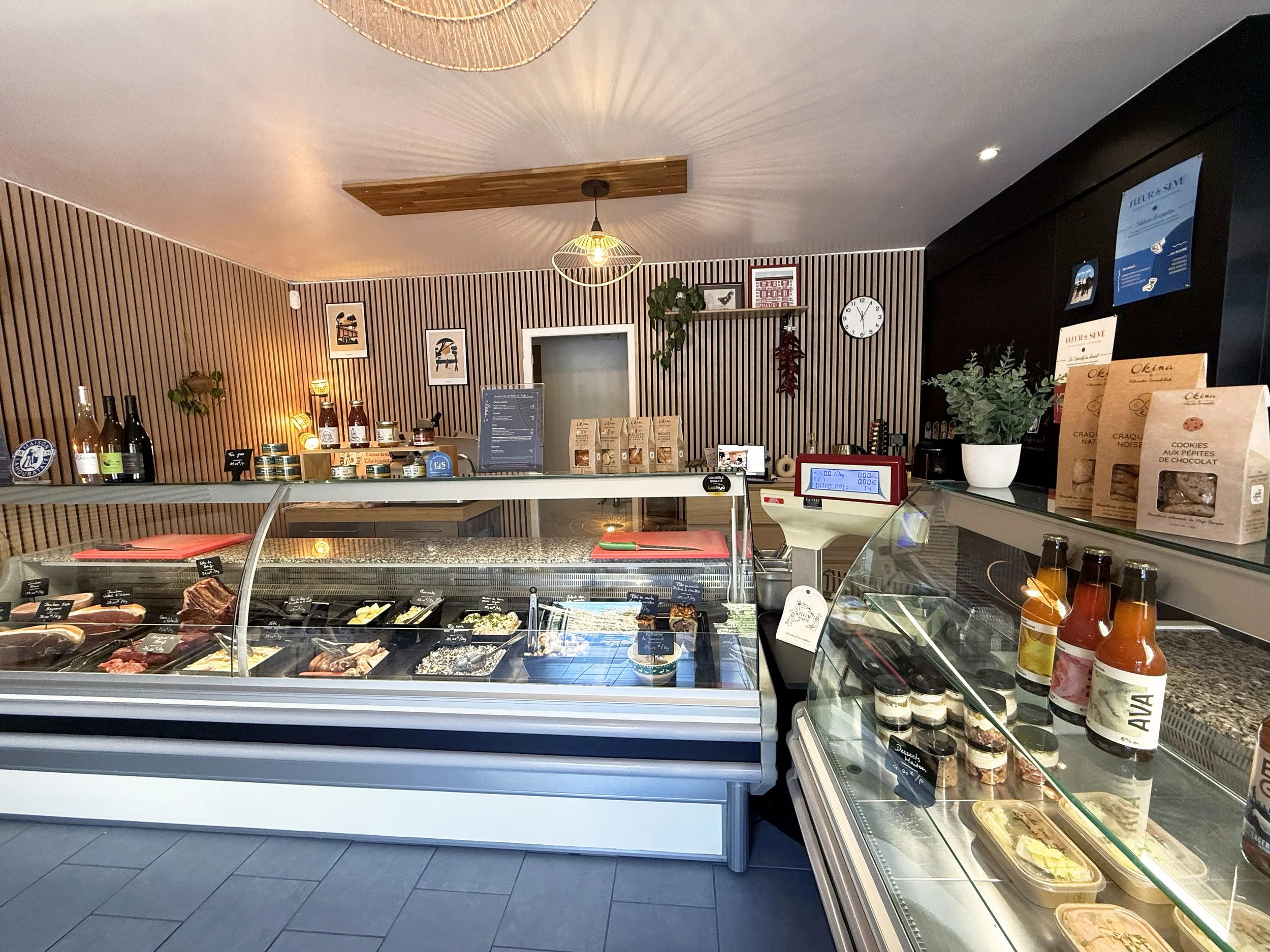 Vitrines de la boutique remplies de produits alimentaires avec des viandes, plats au kilos et boissons, dans une ambiance chaleureuse avec un mur en bois et une décoration moderne.