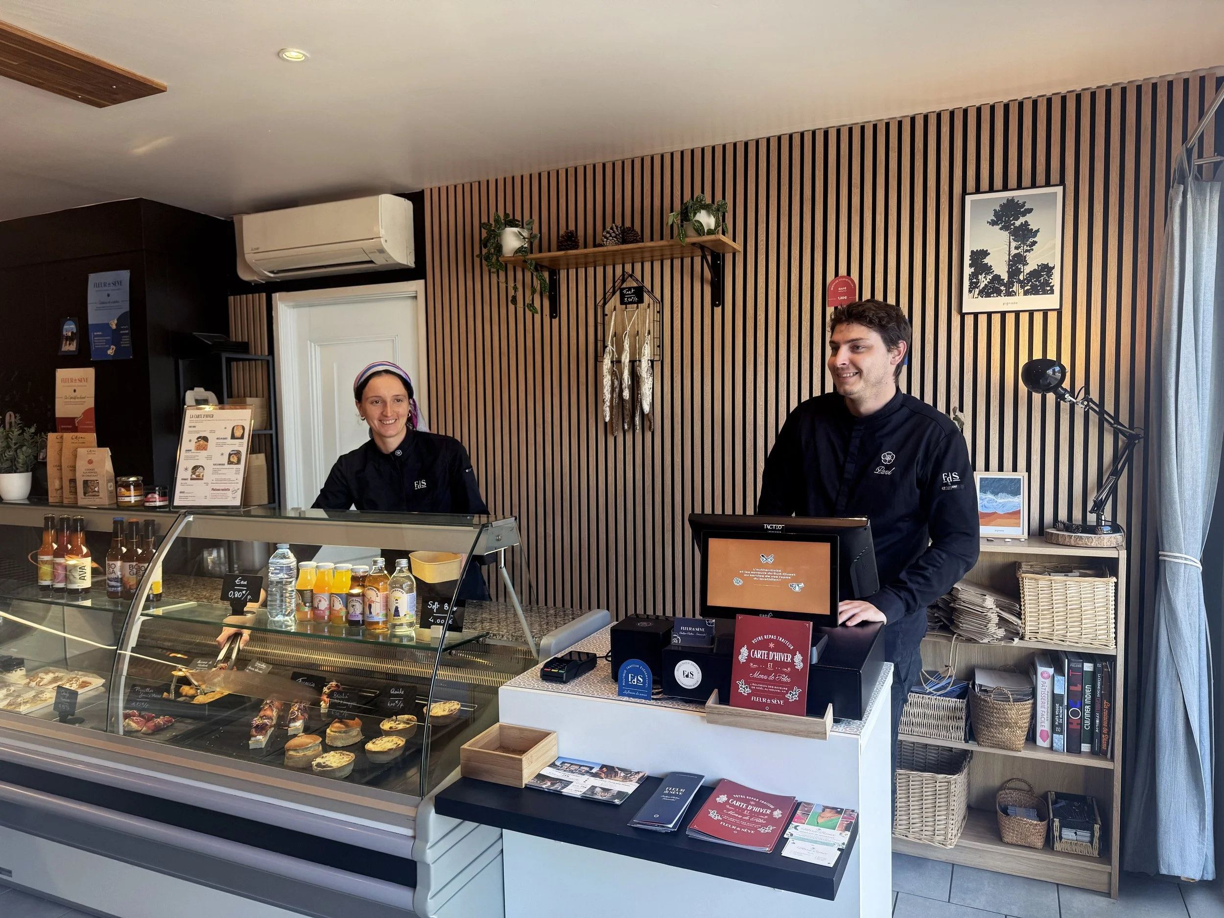 Le chef et l'hôtesse d'accueil derrière la vitrine réfrigérée, souriants.