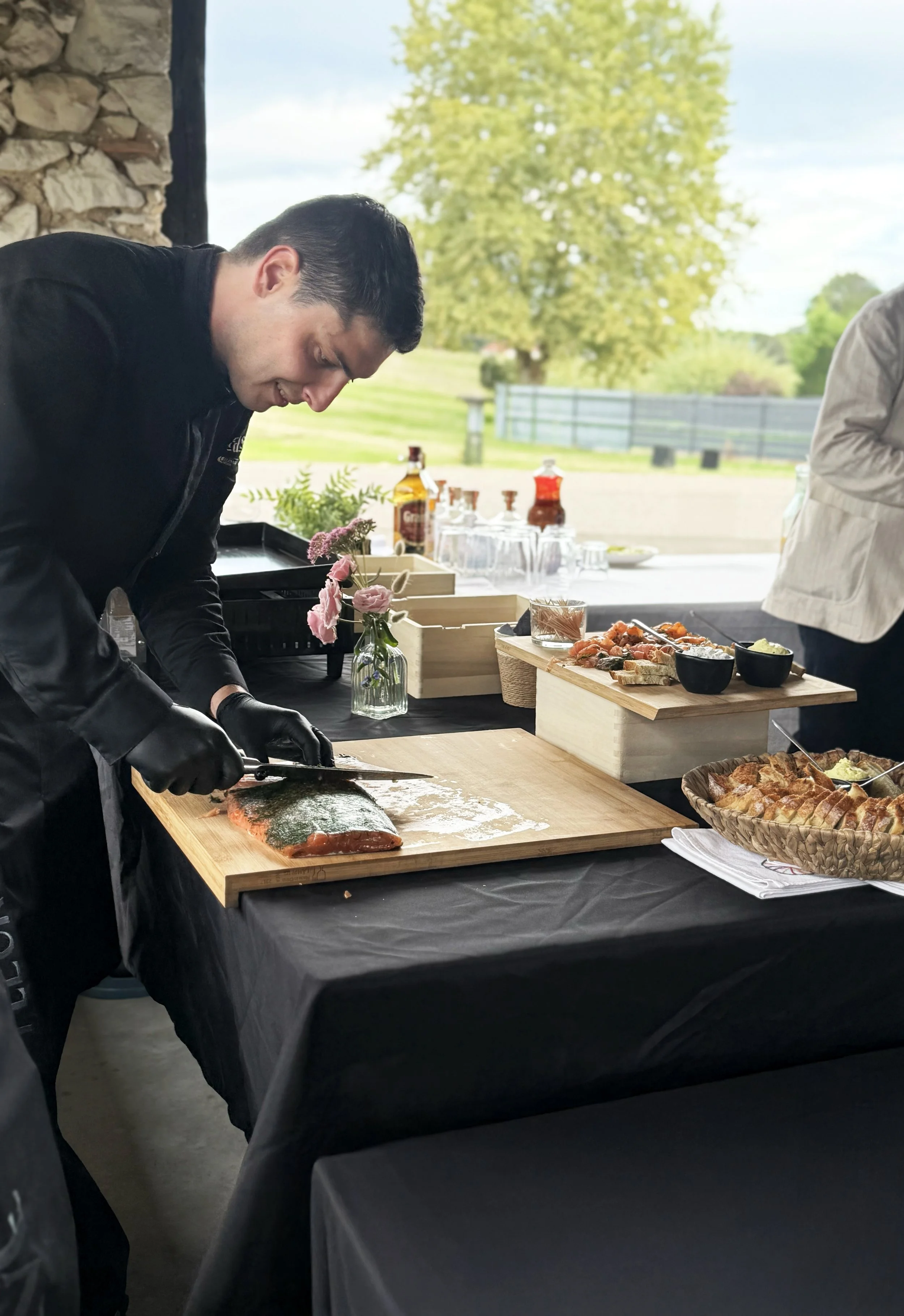 Un chef découpe le saumon gravlax sur une planche à découper lors d'un cocktail d'un mariage au sein d'un paysage verdoyant.