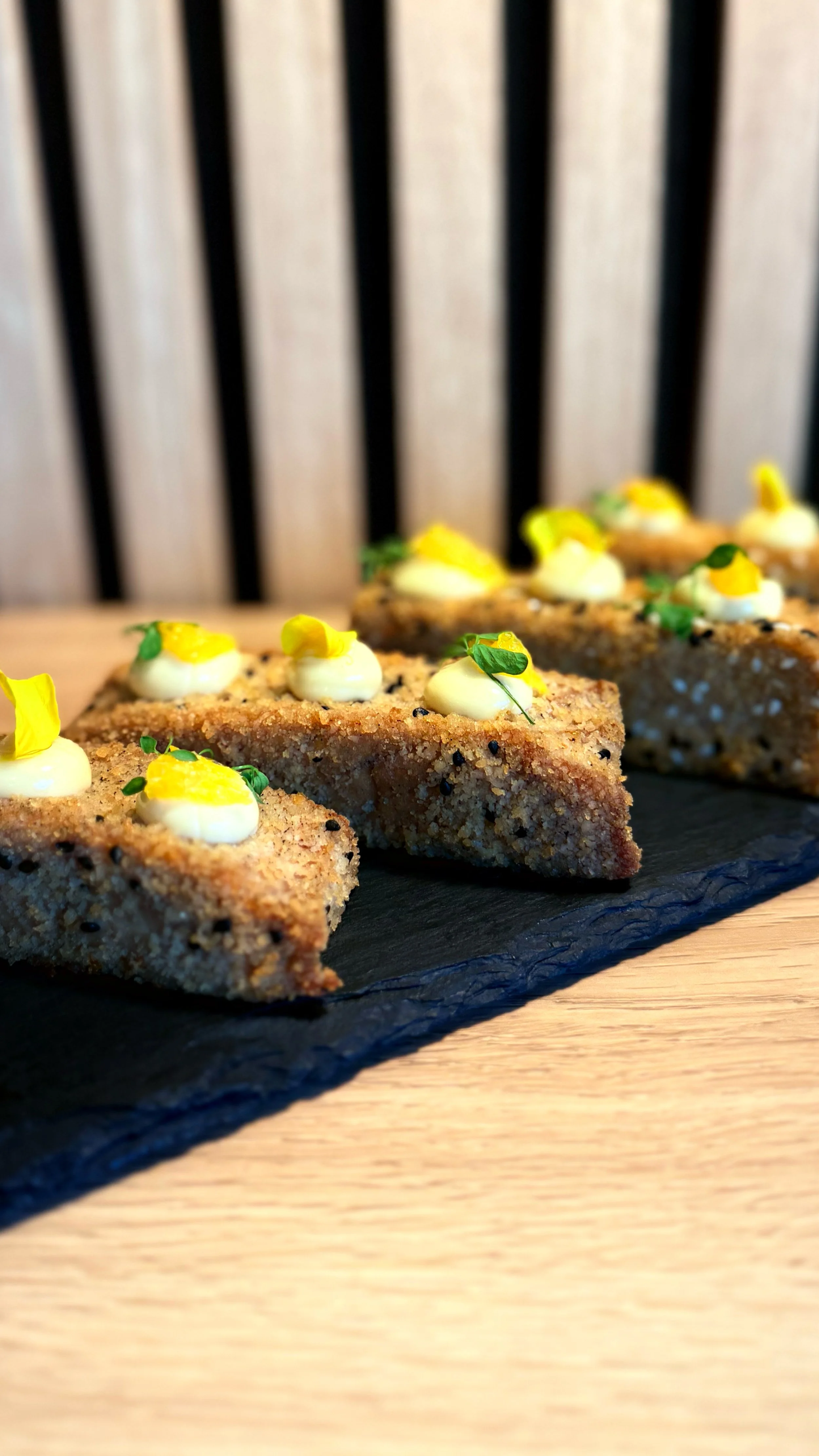 Tataki de thon, mayonnaise maison, agrume et pousses vertes, présentées sur une plaque en ardoise sur une table en bois.