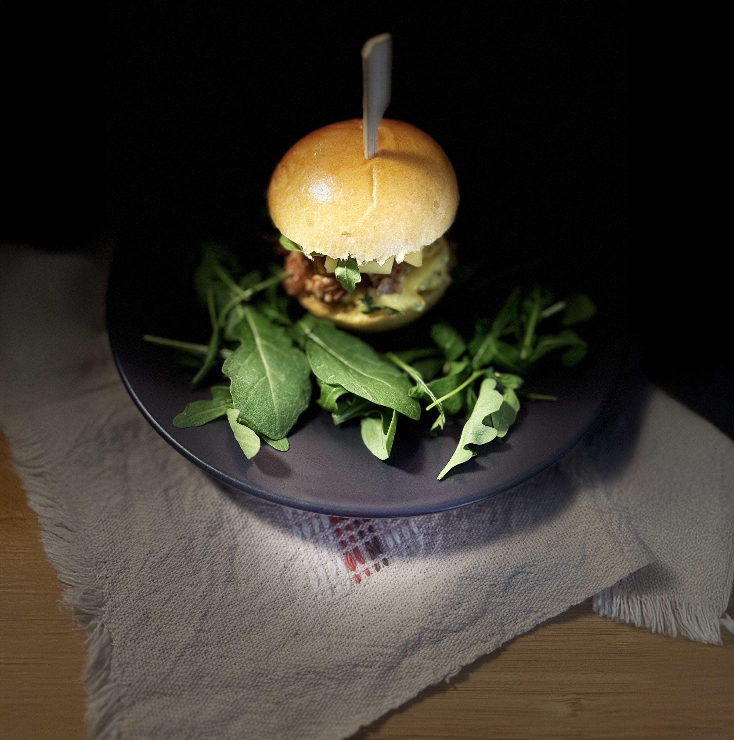 Mini burger avec des feuilles de roquette sur une assiette noire.