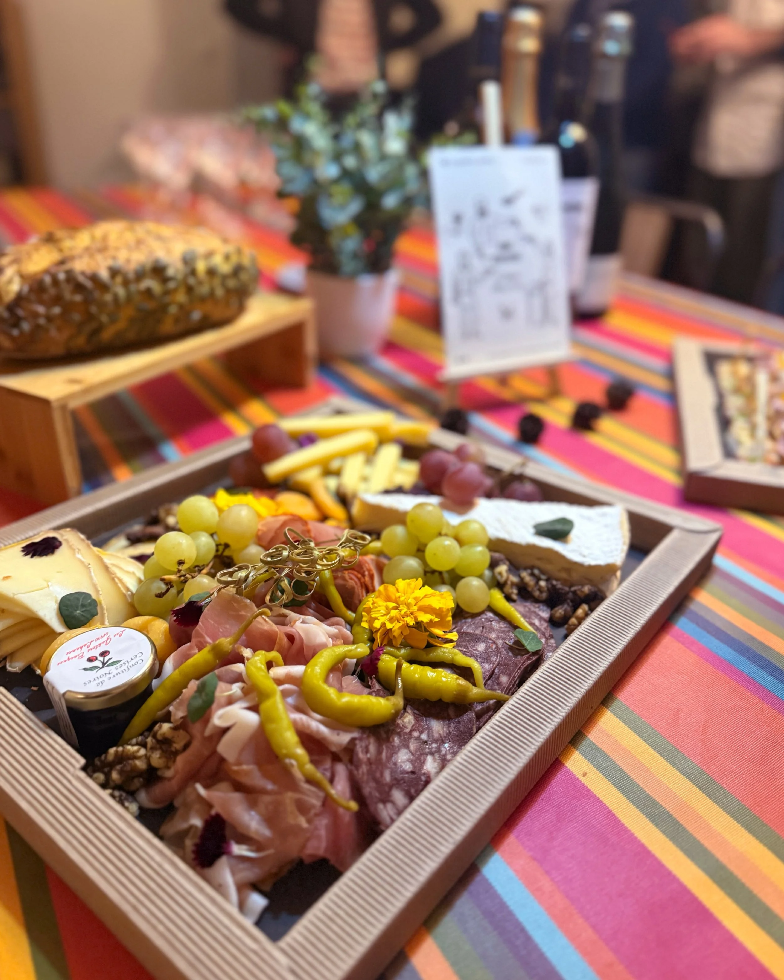 Plate de charcuterie avec fromages, raisins, guidinllas et décoration florale, sur une table colorée.