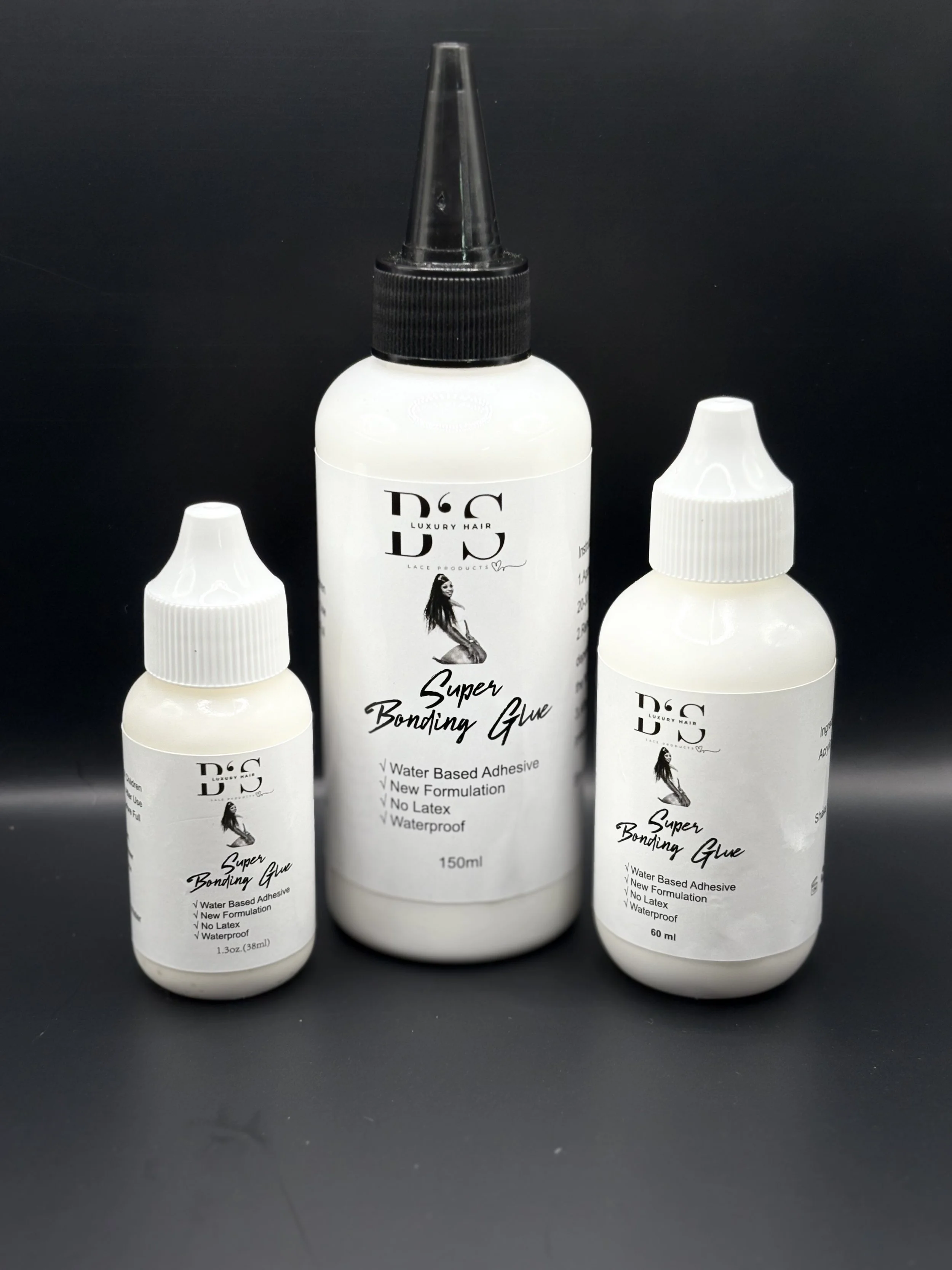 Three bottles of super bonding glue on a black surface, with the middle bottle being the largest and the two smaller bottles flanking it, all labeled B'S Luxury Hair Super Bonding Glue.