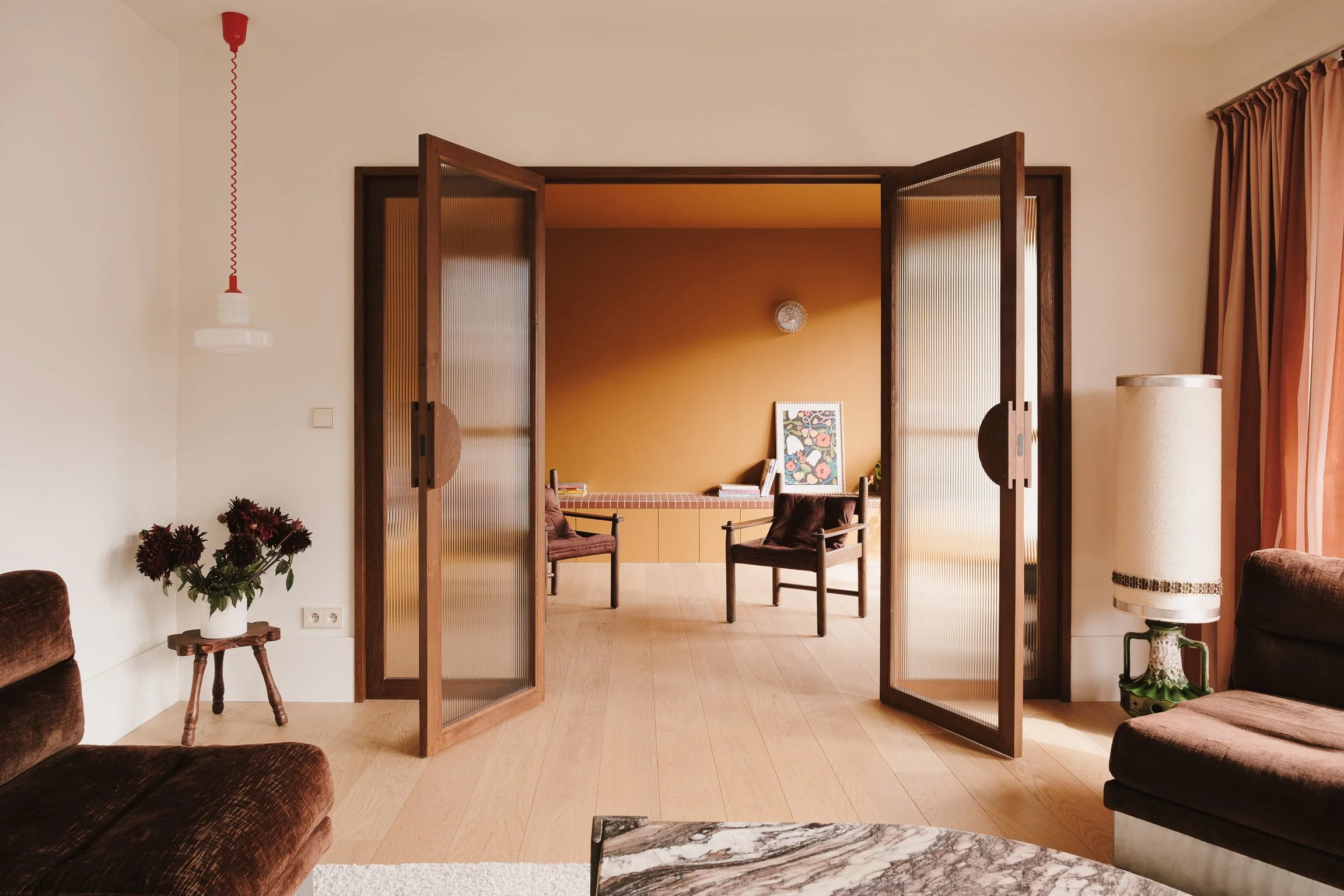 Architecture d'intérieur : perspective sur une enfilade avec menuiserie bois sur mesure, verre texturé et banquette carrelée dans un appartement rénové.