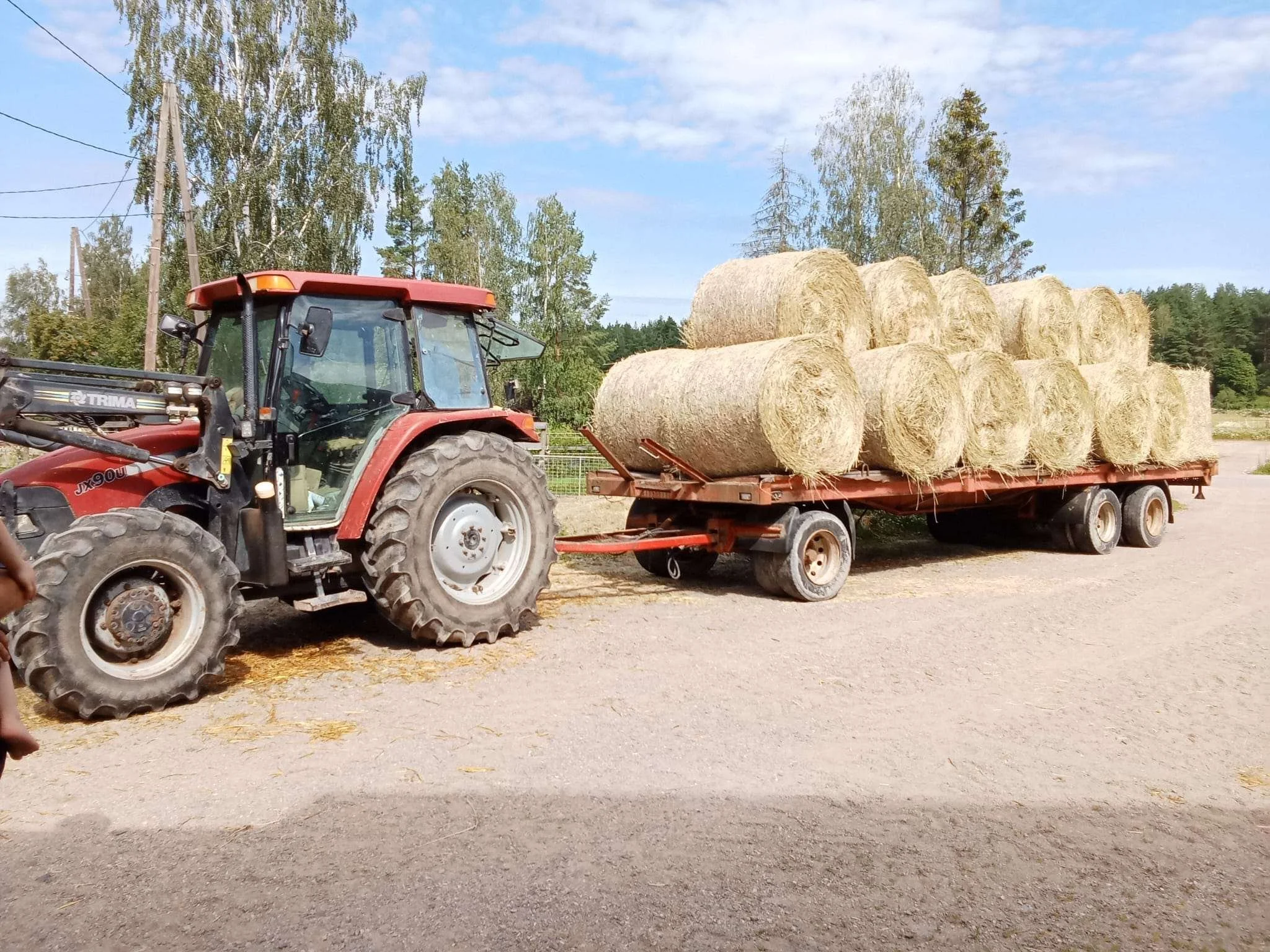 Punainen traktori jonka perässä kärryllinen täynnä olkipaaleja
