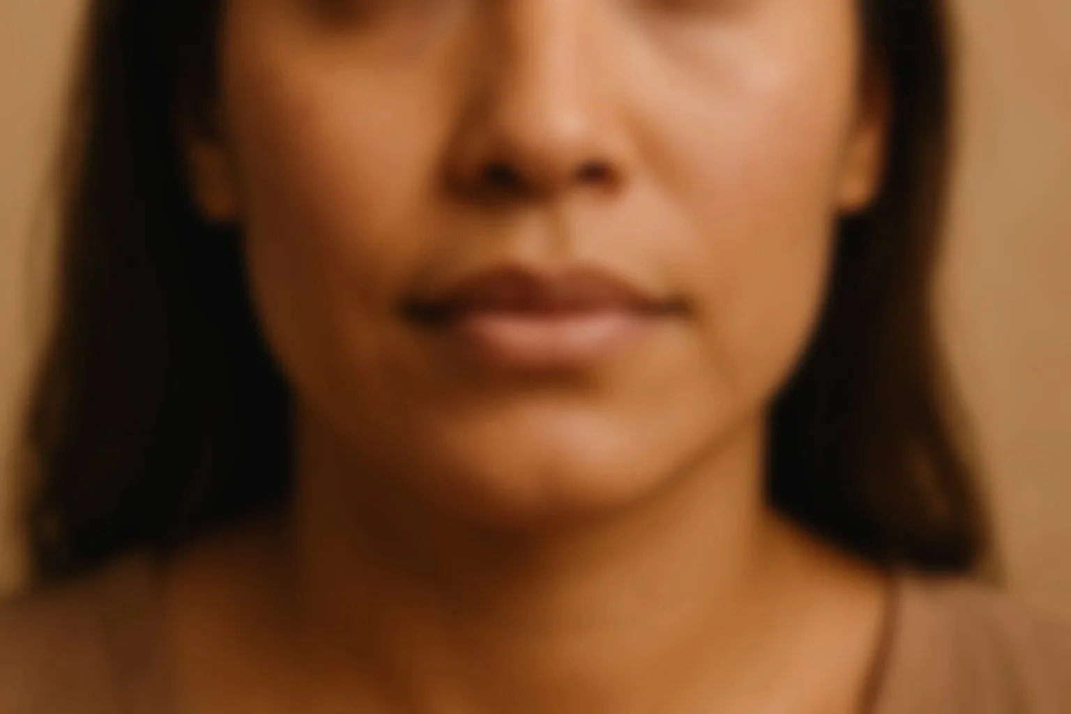 Close-up of a woman's face, showing her lips, nose, and part of her cheek and chin, with dark hair and a neutral background.