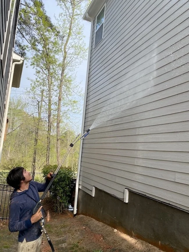 Person using a pressure washer to clean the exterior siding of a house.