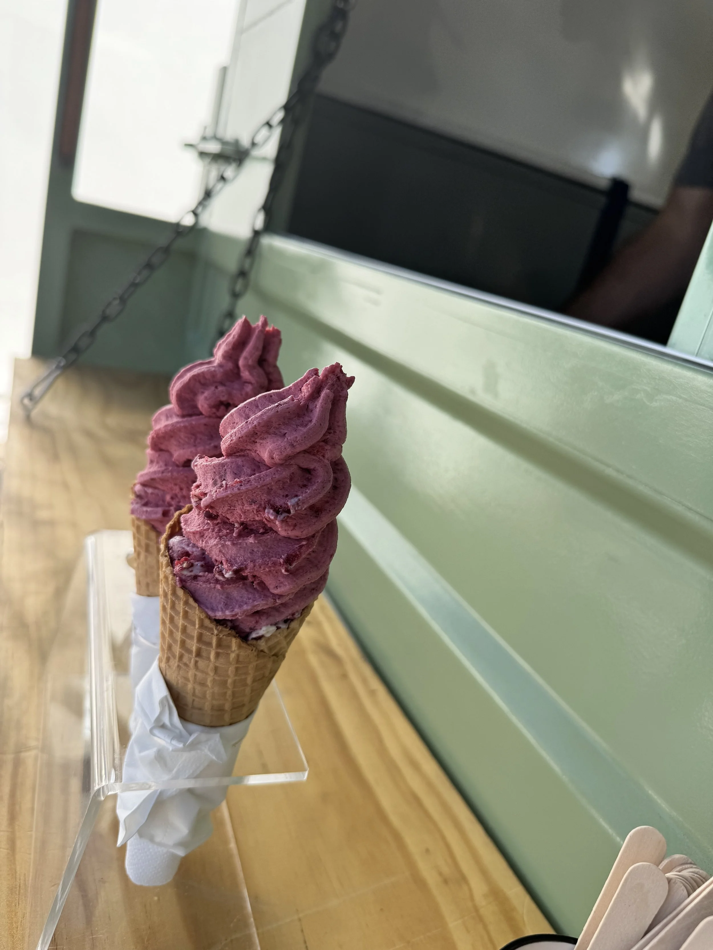 Two pink-dyed soft-serve ice cream cones in waffle cones on a clear stand.